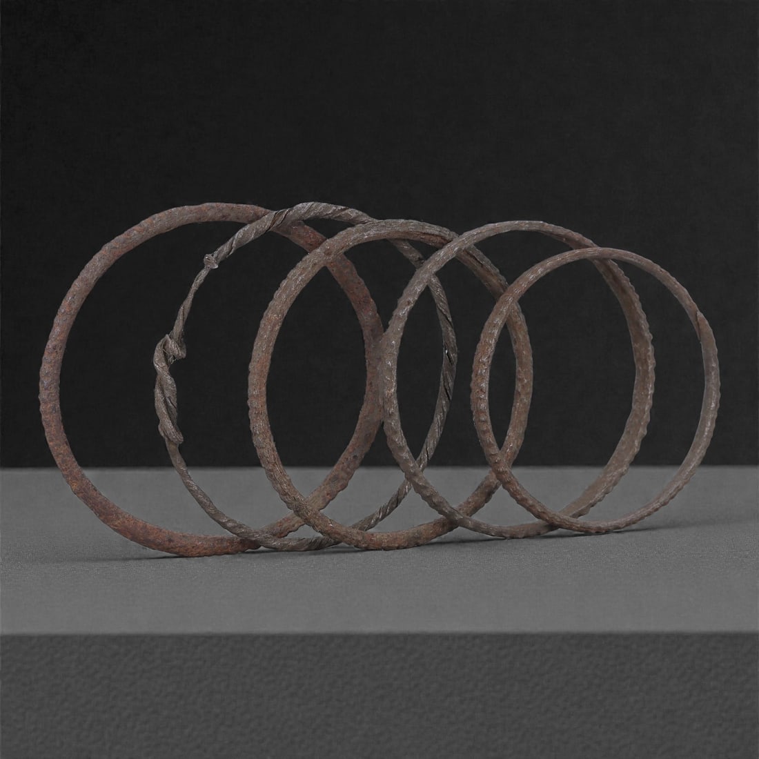 A Group of Roman Iron Bracelets, 1st-3rd Century CE, 71H: Forged from iron strips or rods shaped into open circular bands, the group comprises five bracelets exhibiting rounded to slightly flattened cross-sections. Several pieces show twisted or lightly face