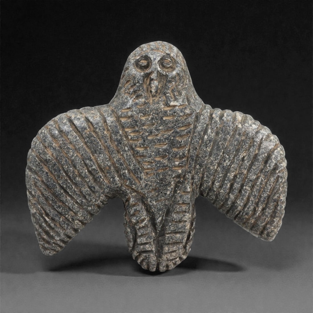 A Levantine Schist Vulture Amulet, Iron Age II, 9th-7th Century BCE, 97LJ: Carved from dark grey schist, the figure depicts a bird of prey with wings extended downward and flanking the body. The head is rounded with drilled circular eyes and a short beak indicated by incised