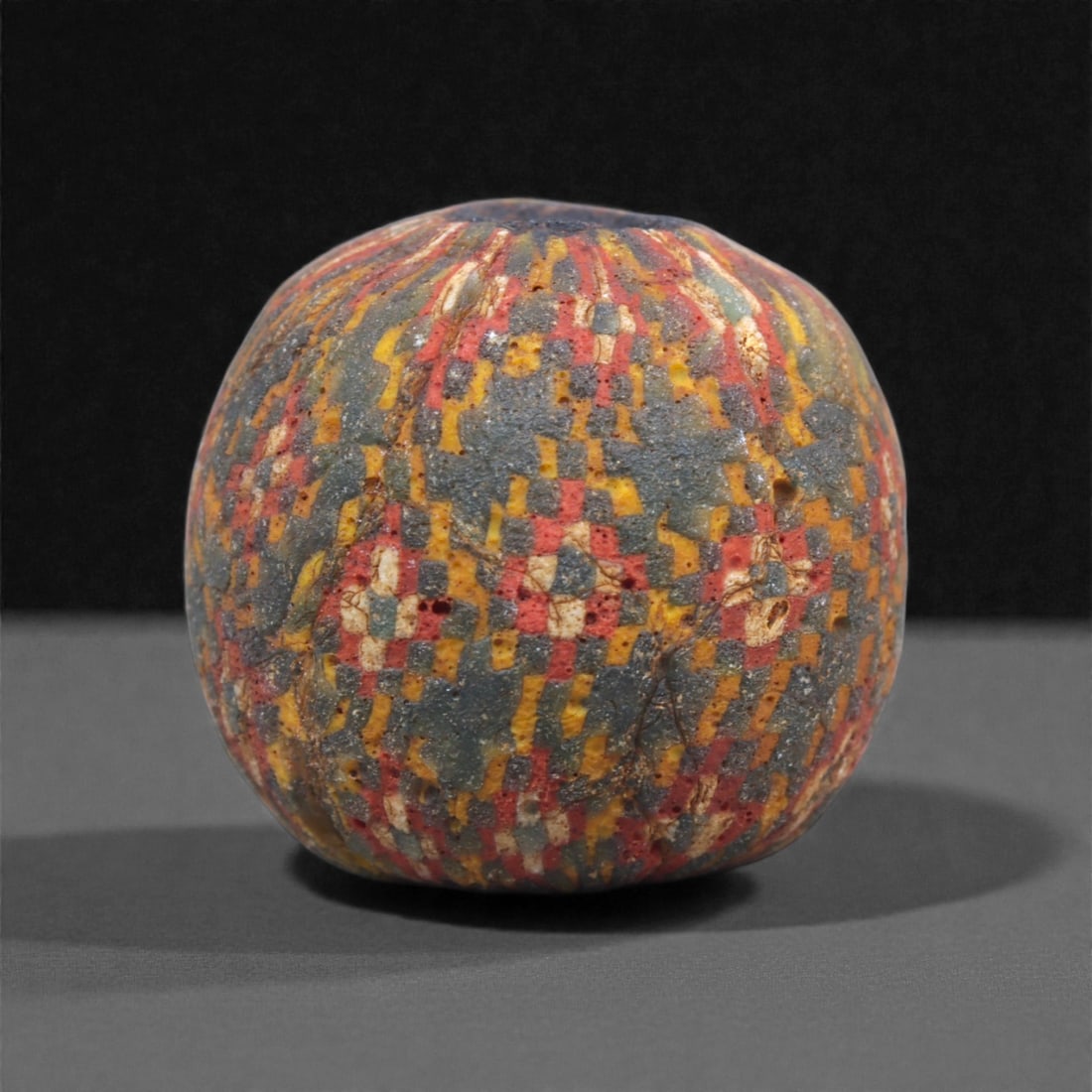 Ancient Egypto-Roman Mosaic Glass Bead - Dense Checker Cane Sphere, 21J: Composed of multicolored mosaic glass, this bead features a tightly packed arrangement of millefiori cane slices forming small checker-patterned units in red, yellow, white, and blue. The canes are al