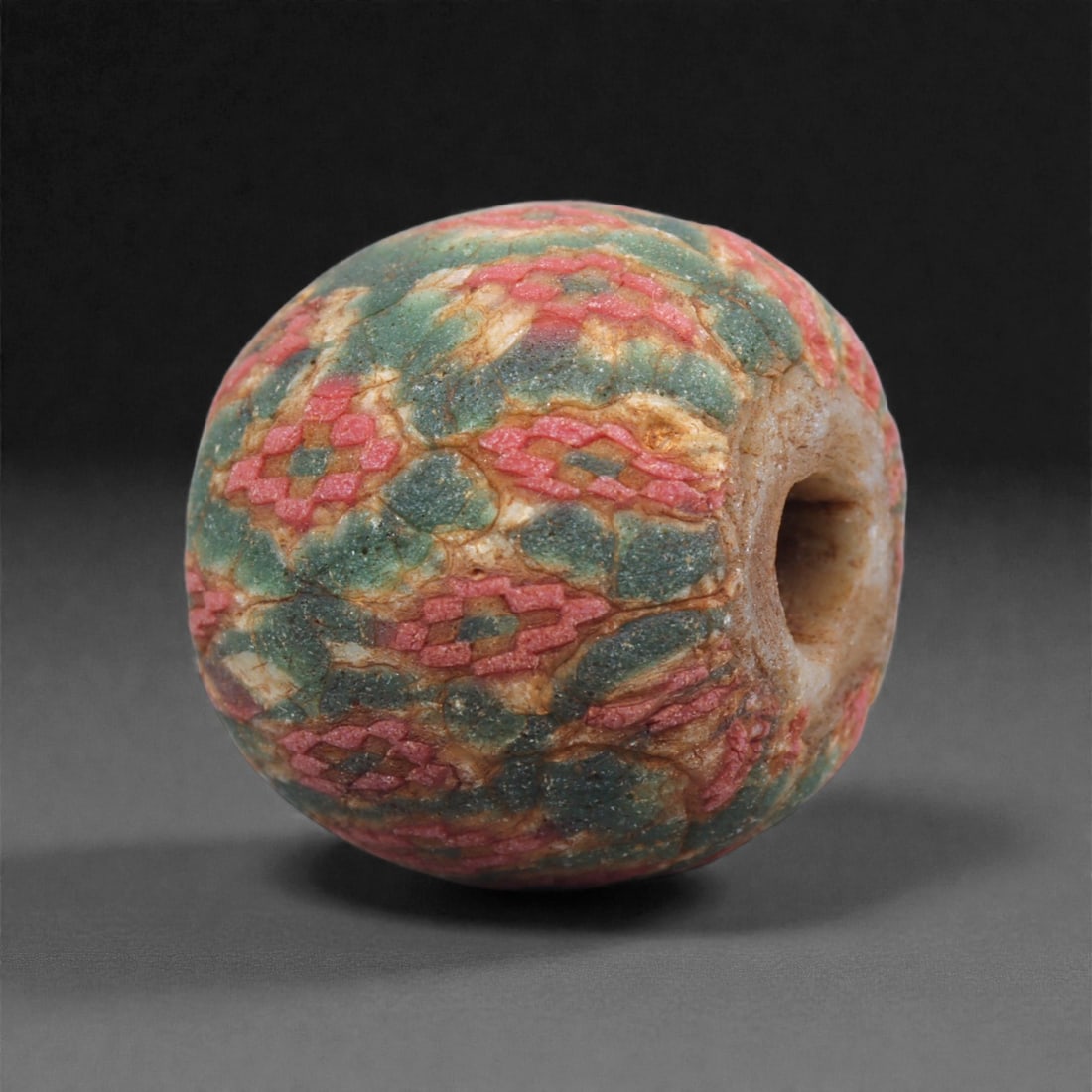 Ancient Egypto-Roman Mosaic Glass Bead - Red-Green Millefiori Cube-Form, 50J: Worked in multicolored mosaic glass, this bead presents a softly squared, cuboid profile formed from tightly fused millefiori canes arranged in repeating vertical bands. The canes display elongated re
