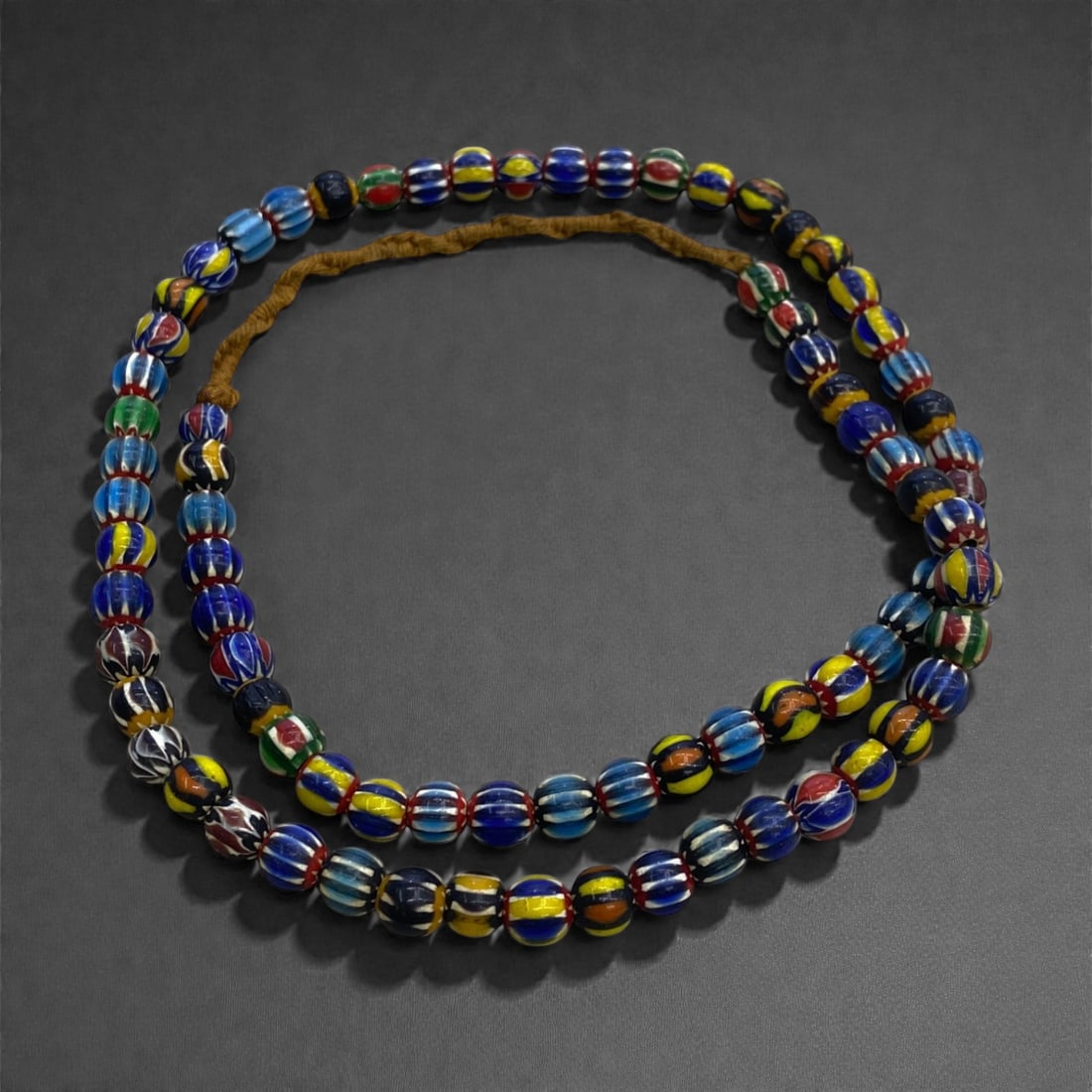 A Venetian Glass Trade Bead Strand, Late 19th-Early 20th Century, 41g, 42AA: Composed of hand-drawn and hand-finished glass beads strung as a continuous strand, the assemblage consists predominantly of small spherical beads decorated with longitudinal marvered striping in poly