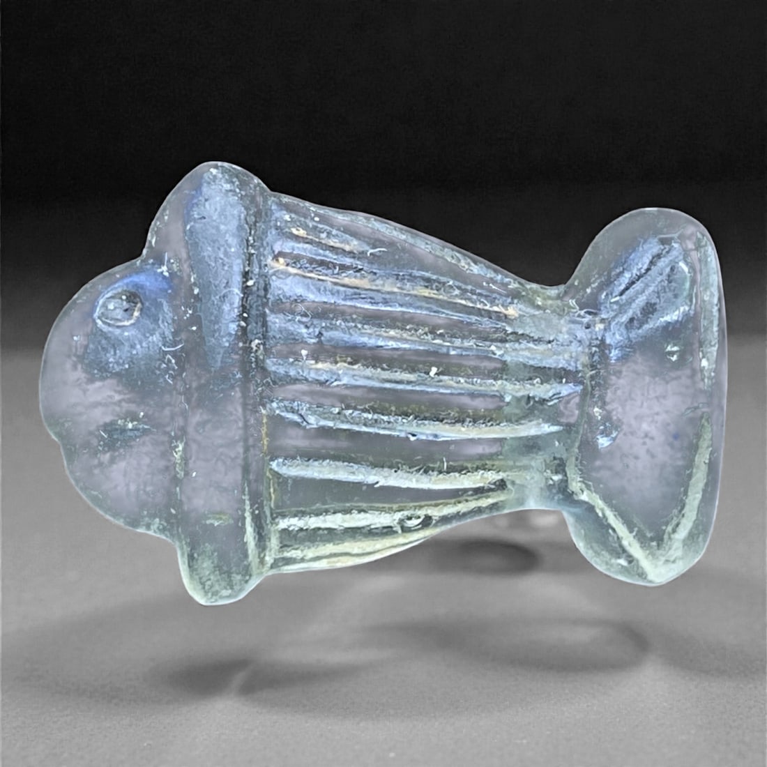 An Ancient Glass Fish Amulet, Late Antique Period, 7g, 73AA: Mold-formed from translucent pale blue glass, this small amulet is shaped as a stylized fish shown in profile. The body is compact and symmetrical, with the head and tail rendered as rounded terminals