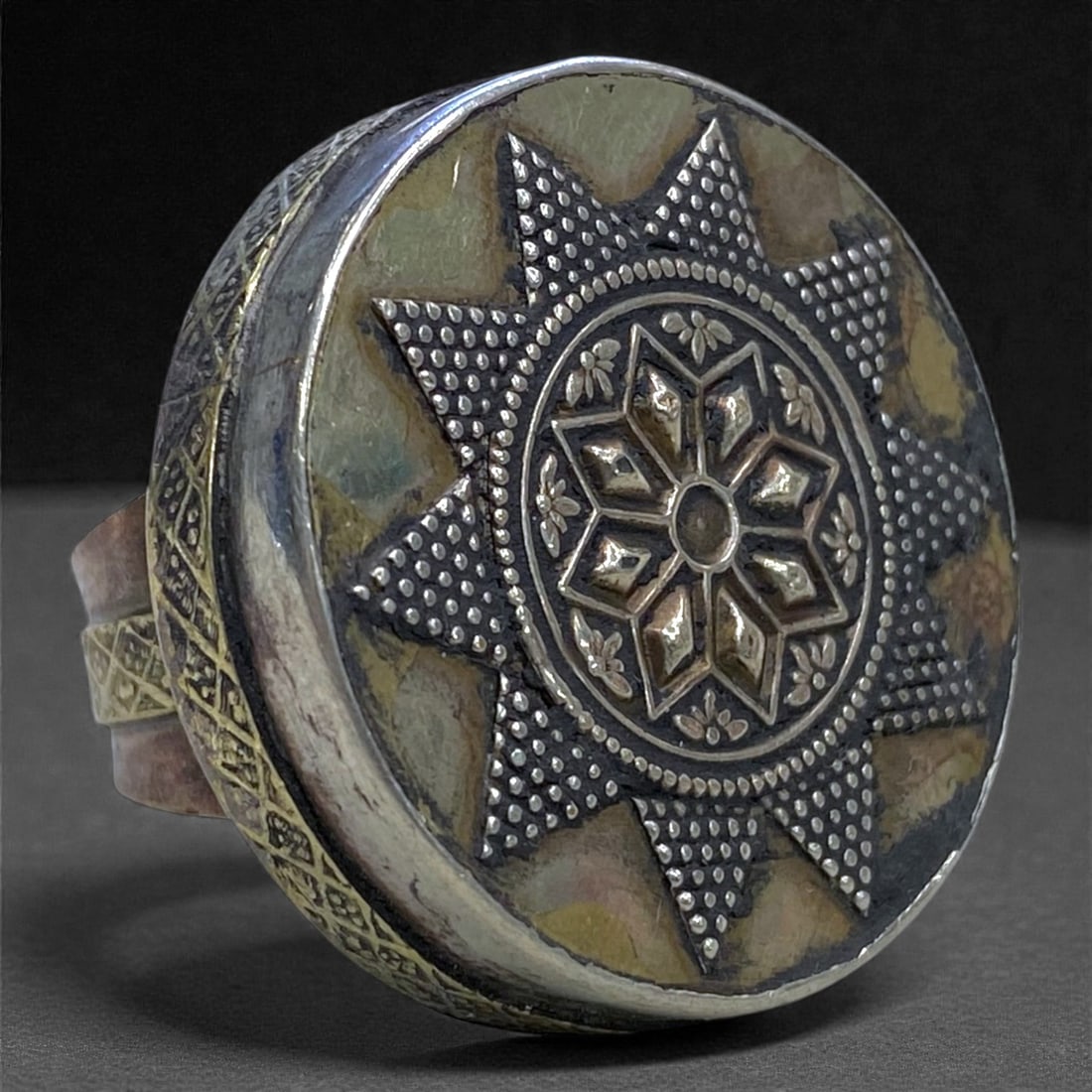 An Islamic Silver Ring with Geometric Rosette and Granulation, 20th Century, 21g, 70AA: Constructed from silver with applied granulation and repousse decoration, the ring is formed with a broad circular bezel dominating the upper surface. The bezel is centered by a raised geometric roset