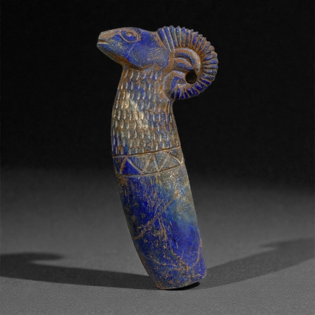 An Achaemenid Lapis Lazuli Ram-Head Finial, Circa 5th-4th Century BCE, 102g, 20AA: Carved from a substantial piece of deep blue lapis lazuli with visible calcite inclusions and areas of iron-rich brown accretion, this sculptural finial is formed as the head and upper neck of a ram, 
