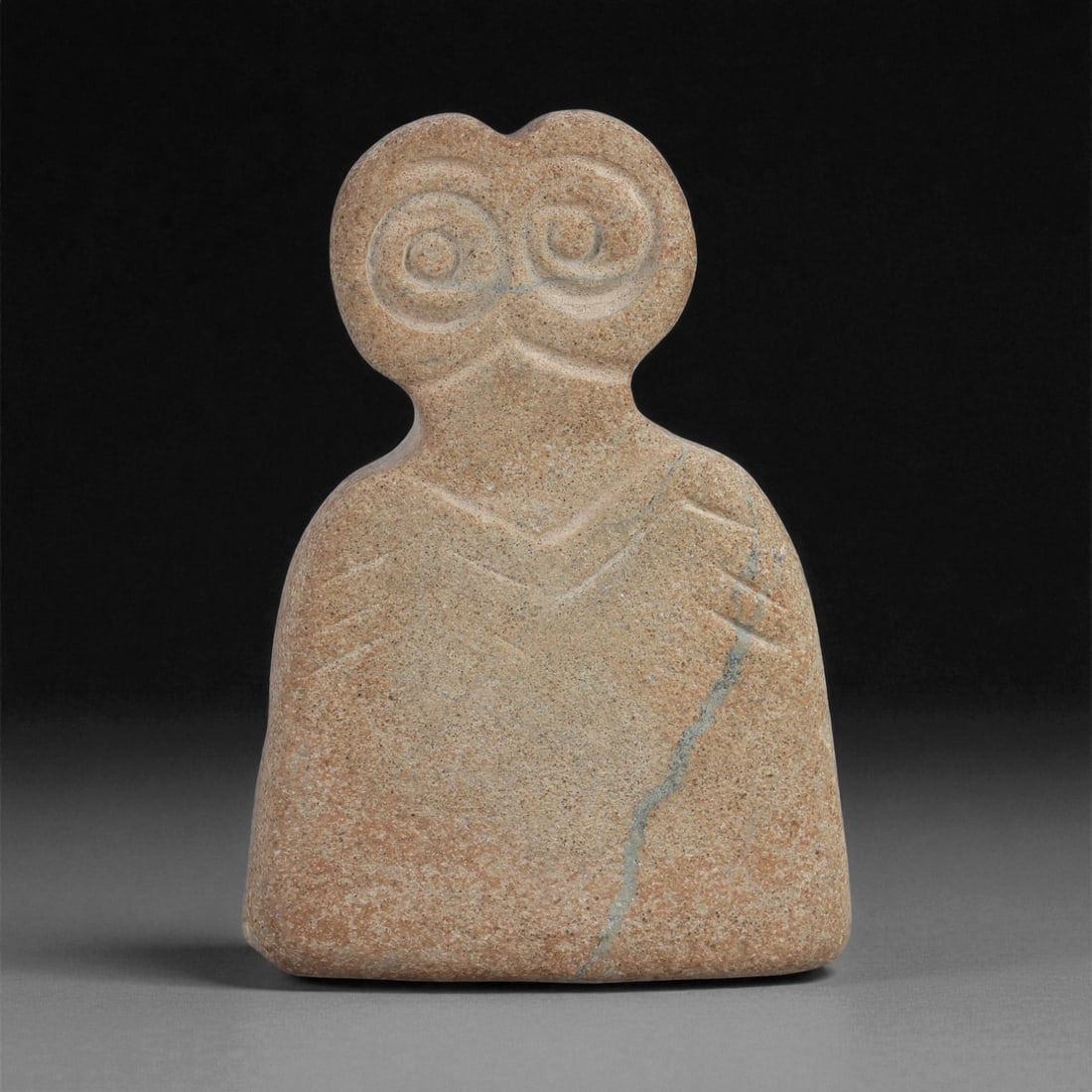A Near Eastern Stone Eye Idol, 4th-3rd Millennium BCE, 66ZB: Carved from a light brown stone with fine surface inclusions and a vertical vein on the lower right, the figure is shaped with a rounded head bearing two recessed circular eyes defined by concentric g