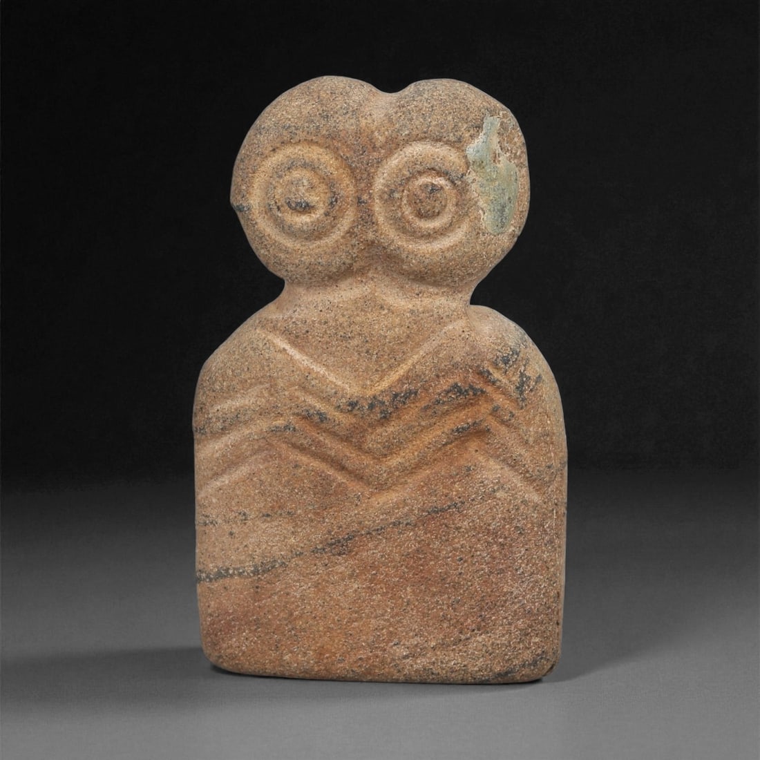 A Near Eastern Stone Eye Idol, 4th-3rd Millennium BCE, 82ZA: Carved from a light brown stone with darker veining and a small area of surface loss on the right side of the head, the figure is shaped with a rounded upper section bearing two recessed circular eyes