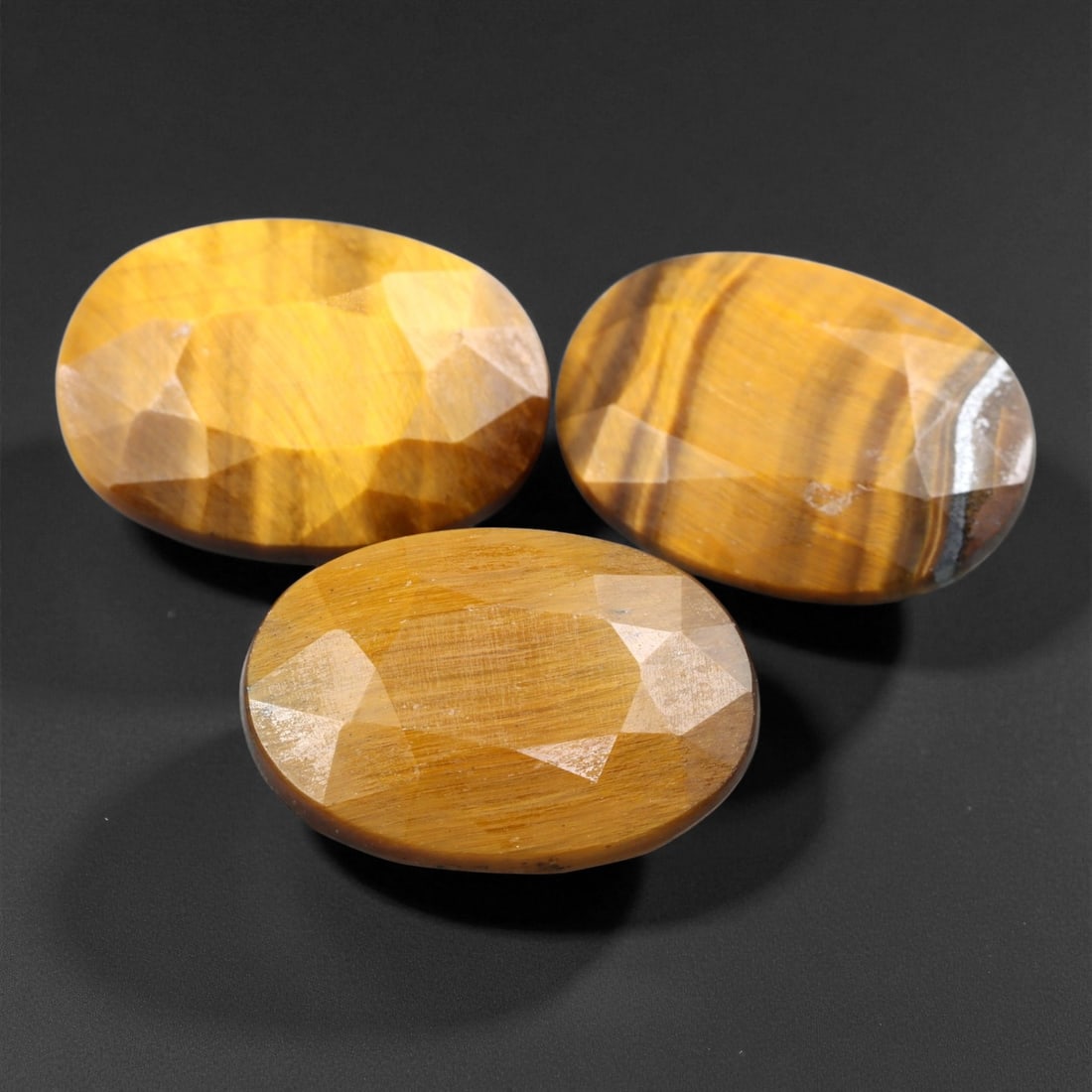 16.75 Carats Golden Brown Tiger Eye Trio - Natural South African Stones - 1.4 cm, 19XE: This trio of faceted tiger eye gems exhibits the signature golden chatoyancy that makes this stone so distinctive, with flowing bands of caramel, bronze, and deep honey hues. The oval shapes are exper