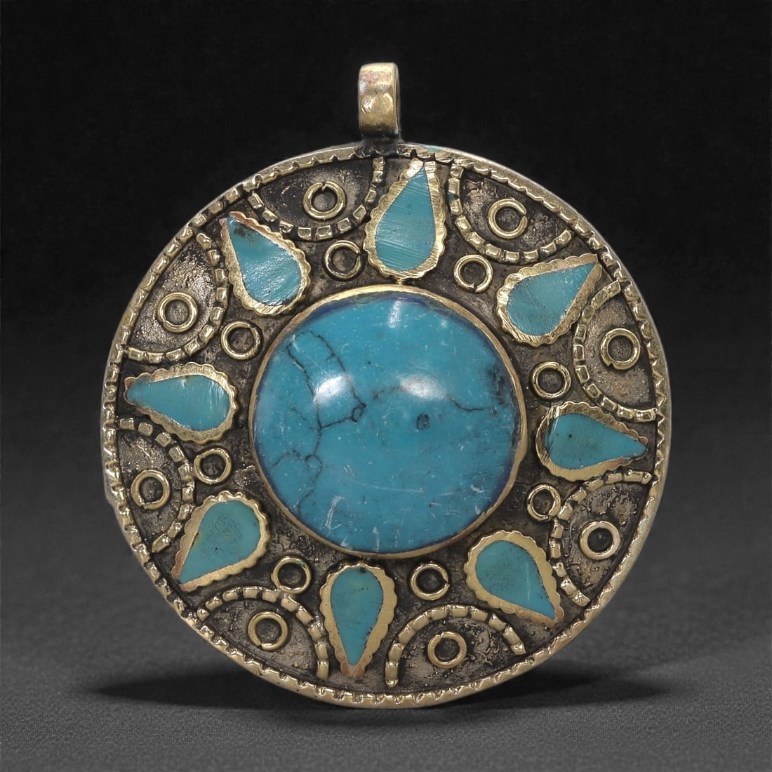 Himalayan Style Brass Pendant - Turquoise Inlay Amulet, 43XF: This circular brass pendant is organized around a large central turquoise cabochon set within a raised collar, its surface showing natural veining typical of the stone. Radiating outward is a ring of