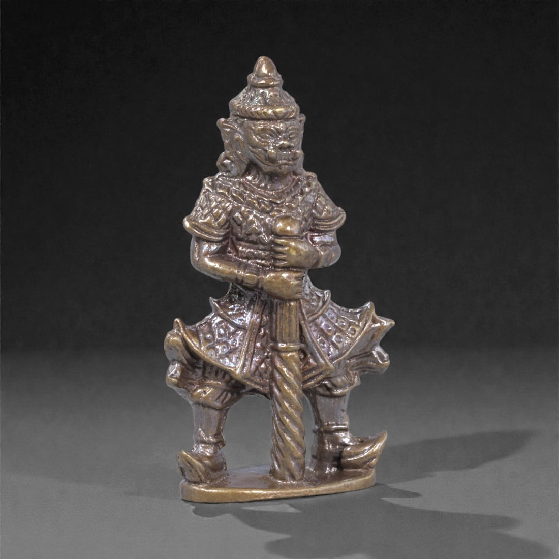Bronze Guardian Warrior Figurine - Southeast Asian Ritual Idol, 54WE: Cast in bronze with careful attention to costume and posture, this small figurine depicts a standing guardian warrior shown gripping a vertical club or staff held against the torso. The figure wears a