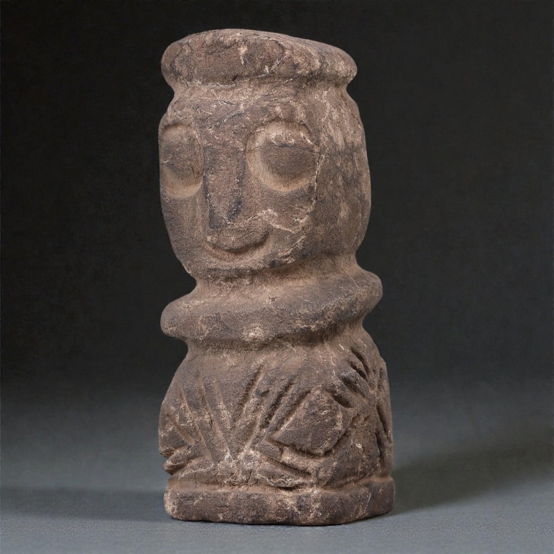 A Near Eastern Stone Anthropomorphic Idol, 4th-3rd Millennium BCE, 20R: Carved from dark brown stone with visible mineral inclusions and areas of surface wear, the object is formed as a compact anthropomorphic idol with a cylindrical body and an integrated head. The face