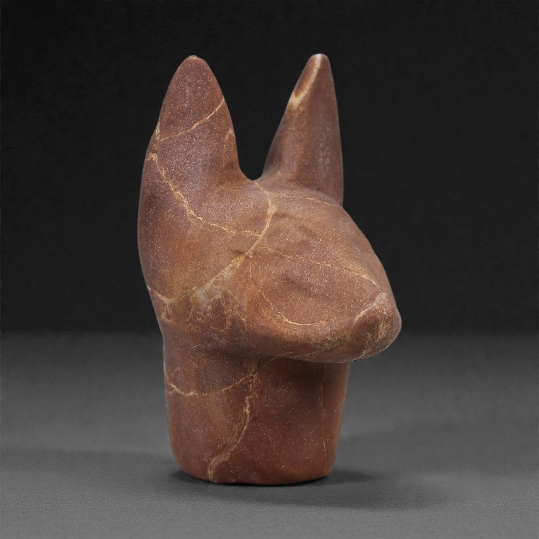 Ancient Stone Canine Head - Zoomorphic Effigy, 62F: Carved from a single piece of fine-grained stone, this small zoomorphic effigy represents a stylized canine head rendered in the round. The form is vertically oriented, with upright ears, an elongated