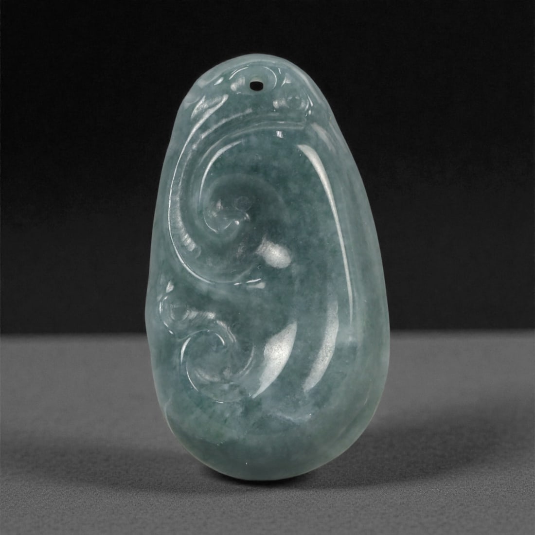 Chinese Jade Amulet - Carved Stone Pendant, 71ZD: Carved from dark green jade with soft translucency and subtle internal mottling, this small amulet is formed as an elongated plaque worked in shallow relief with flowing scroll motifs that emphasize c