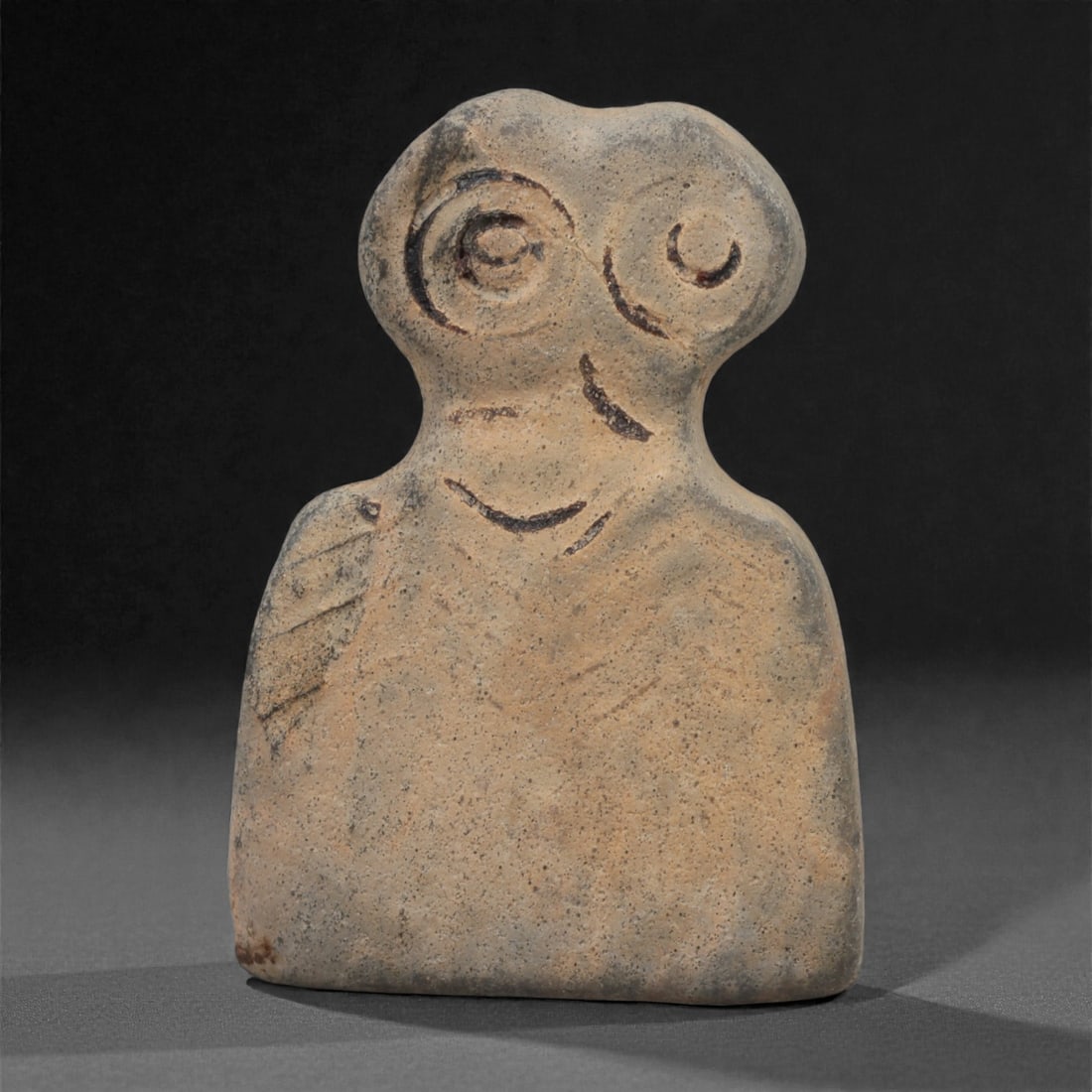 A Northern Mesopotamian Stone Eye Idol, Late 4th Millennium BCE, 47LQ: Carved from a light beige stone with a flattened rectangular lower body, the idol rises to a bifurcated upper section bearing two large circular eyes formed by deeply incised concentric grooves. Addit