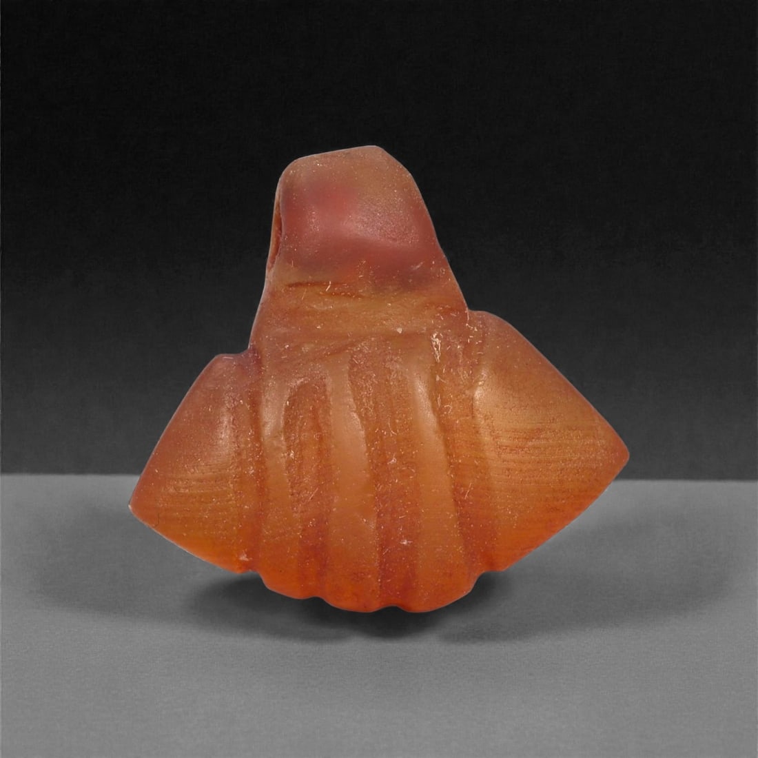 An Egyptian Carnelian Amulet, Coptic Period, 4th-7th Century CE, 1.7cm, 27LJ: Worked from orange carnelian with natural internal variation, the amulet shows a compact form with smoothed contours and modest surface definition. Light wear is visible along the edges. Objects of th