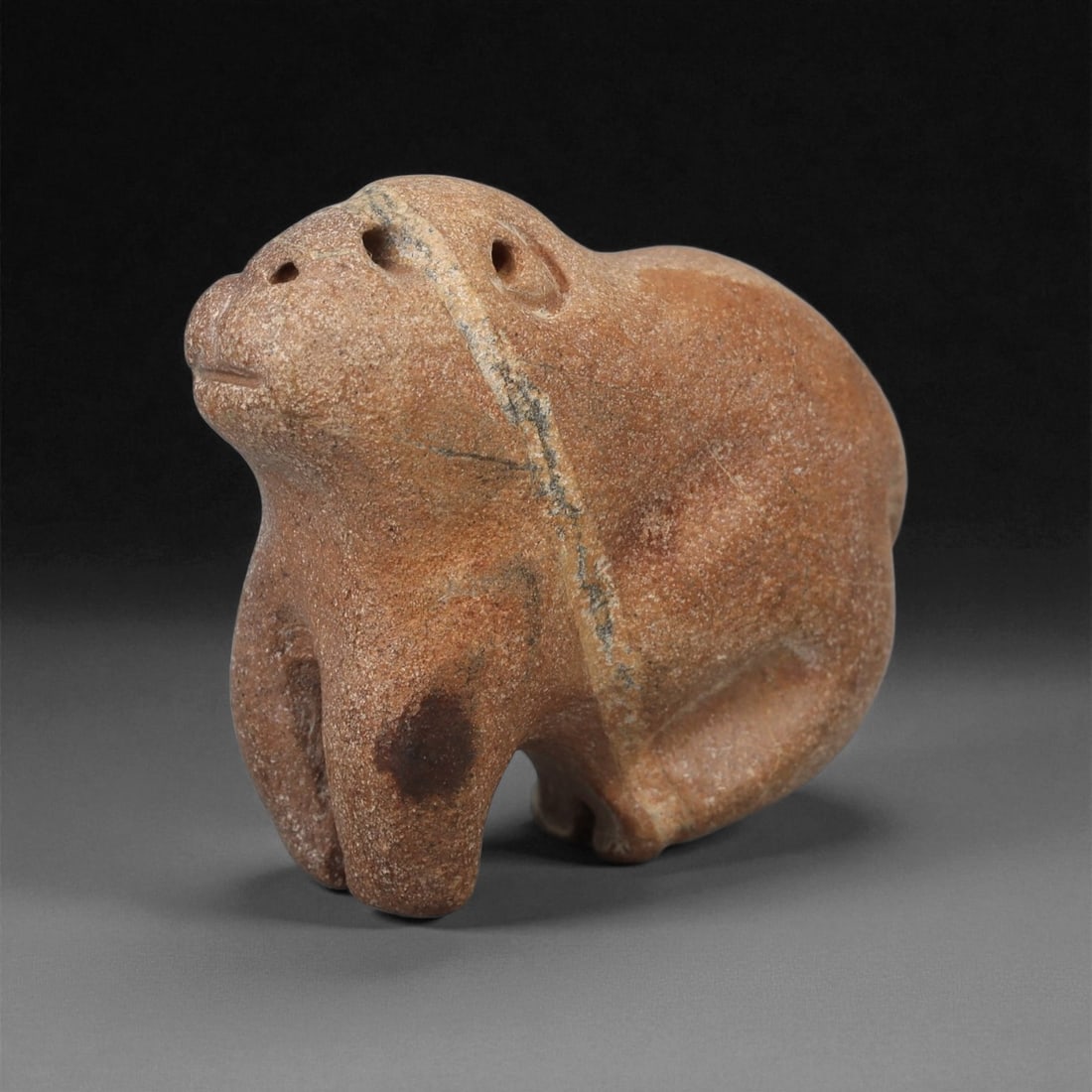 A Near Eastern Stone Zoomorphic Figurine, 3rd-2nd Millennium BCE, 5LA: Carved from brown stone with lighter surface veining, the figure represents a compact quadruped with a rounded body and short legs. The head is raised, with two drilled circular eyes and a shallow inc