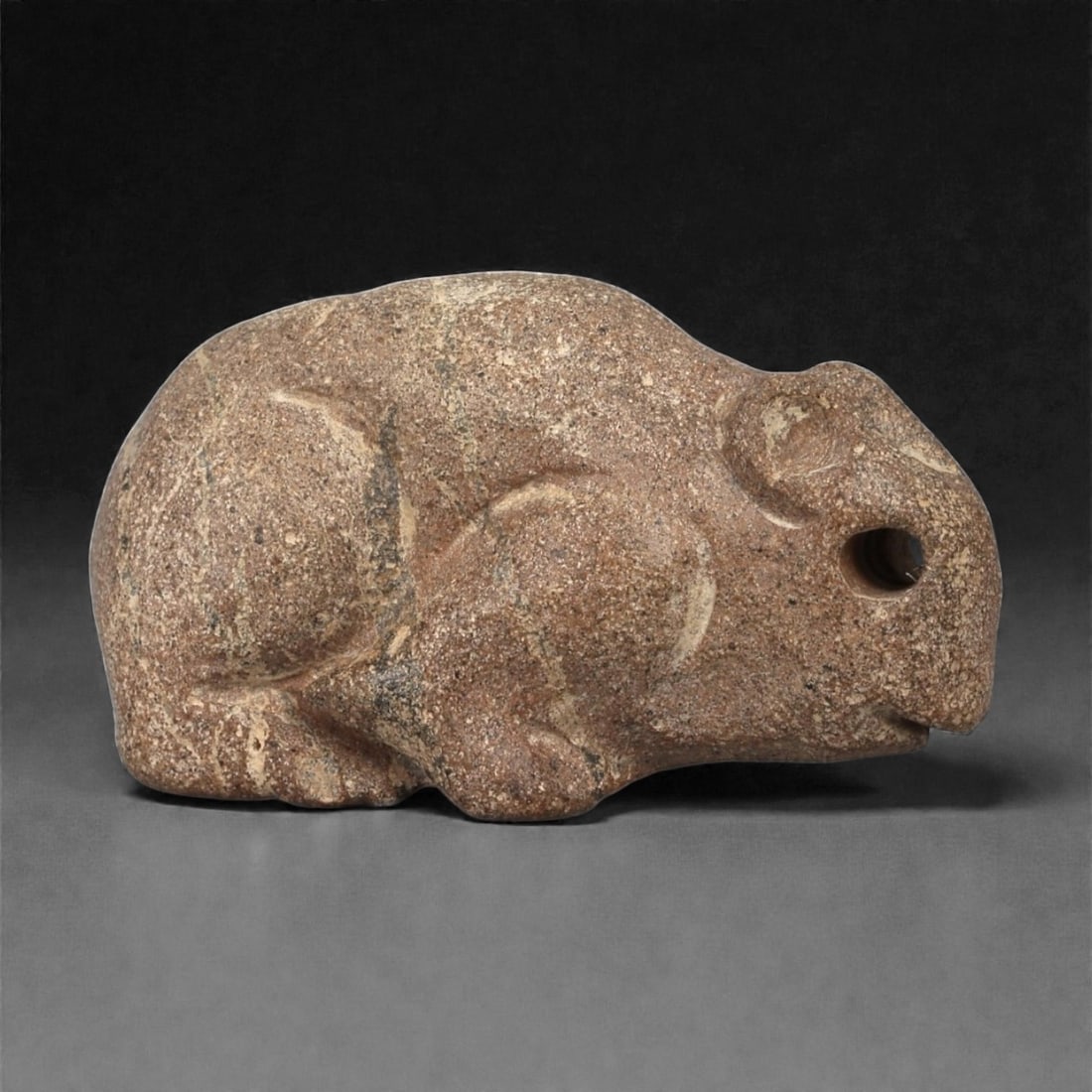 A Near Eastern Stone Zoomorphic Figurine, 3rd-2nd Millennium BCE, 49LB: Carved from a coarse-grained brown stone with lighter veining, the object depicts a small quadruped in a crouched posture. The head features a drilled circular eye and a short, rounded snout. The limb