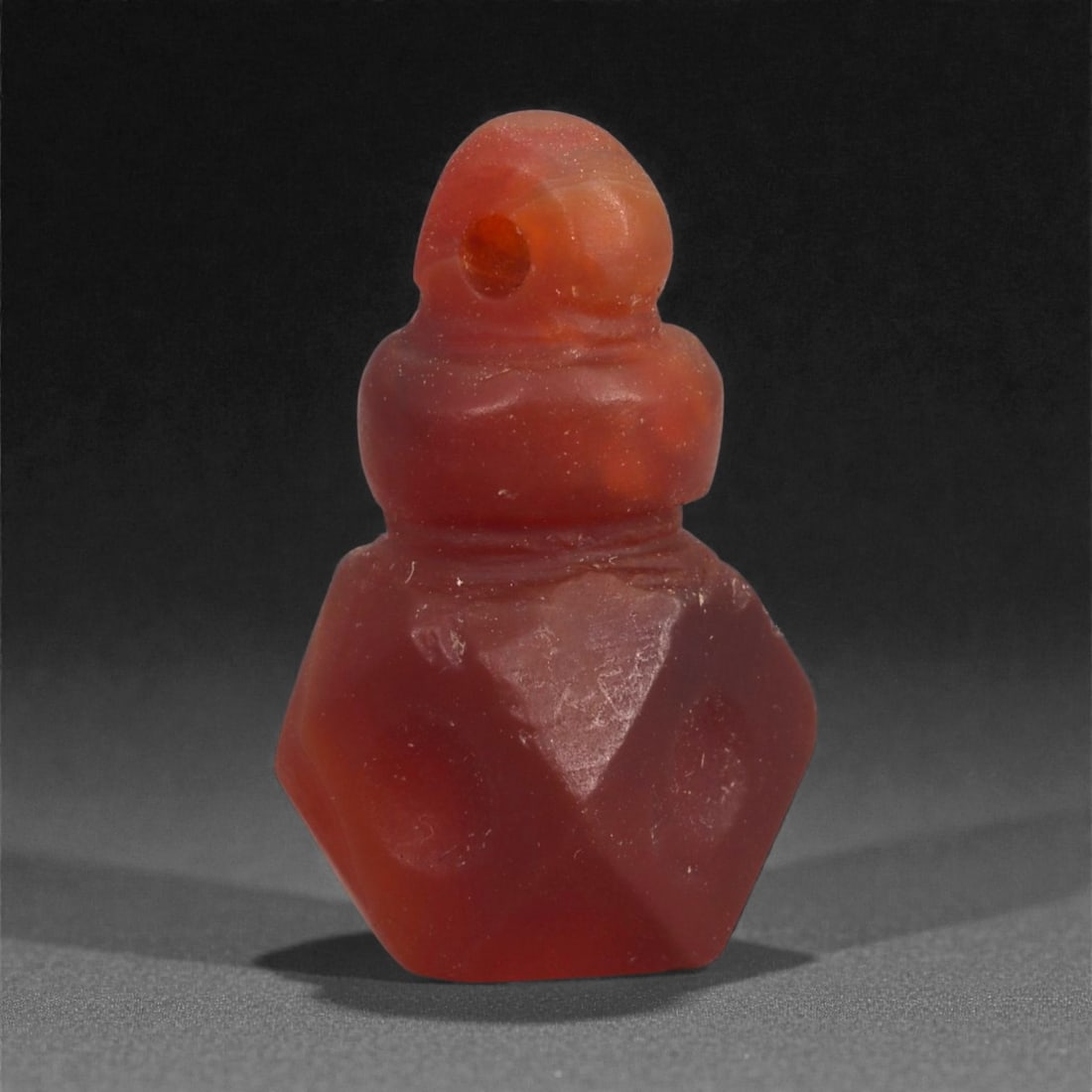 An Egyptian Carnelian Amulet, Coptic Period, 4th-7th Century CE, 2.1cm, 29LJ: Worked from orange carnelian with natural internal variation, the amulet shows a compact form with smoothed contours and modest surface definition. Light wear is visible along the edges. Objects of th