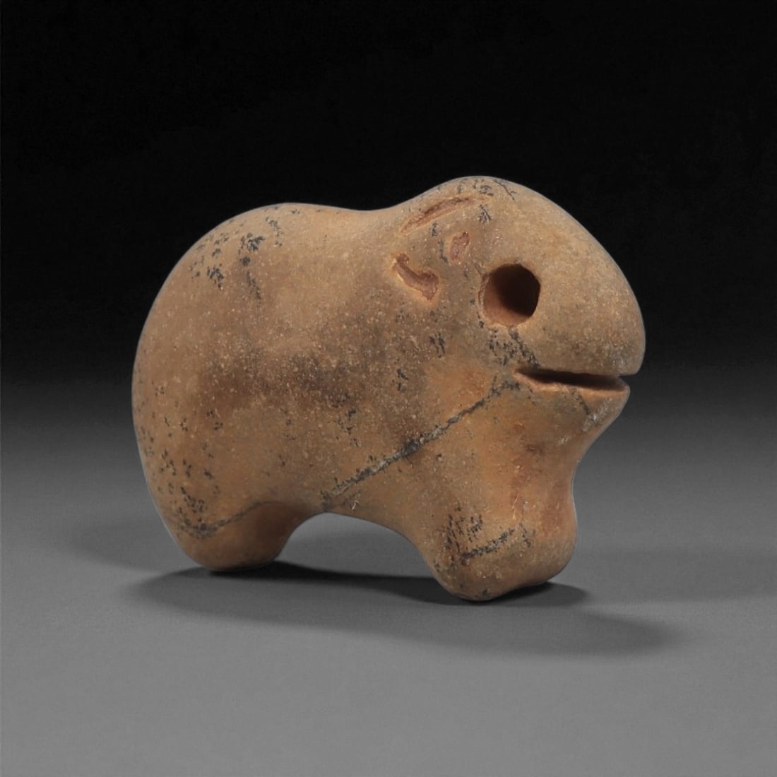 A Near Eastern Stone Zoomorphic Figurine, 3rd Millennium BCE, 2LF: Carved from a light brown stone with darker surface inclusions, the object is shaped as a small quadruped with a rounded body and short legs. The head features a drilled circular eye, a shallow incise