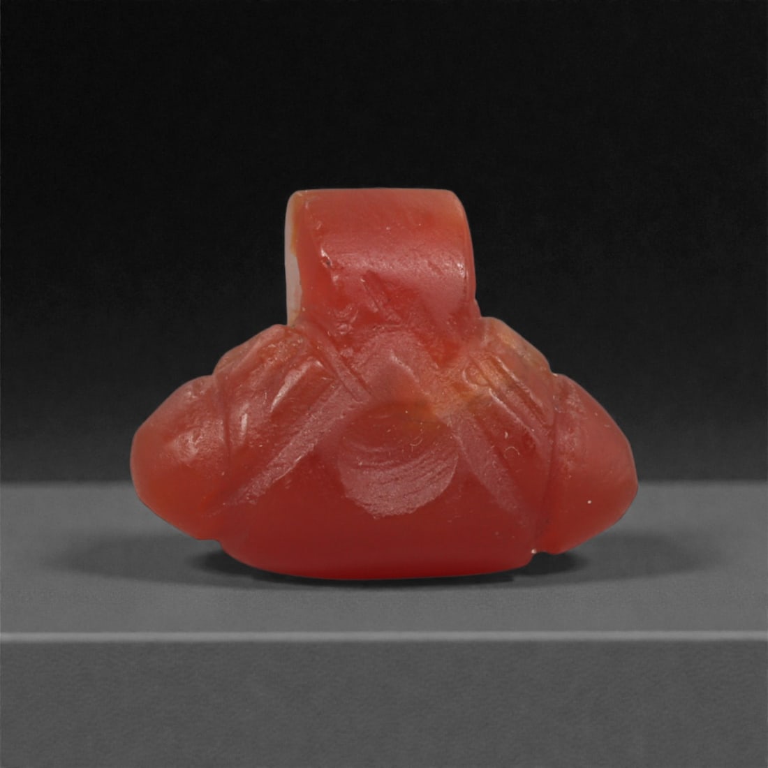 An Egyptian Carnelian Amulet, Coptic Period, 4th-7th Century CE, 1.5cm, 33LN: Worked from orange carnelian with natural internal variation, the amulet shows a compact form with smoothed contours and modest surface definition. Light wear is visible along the edges. Objects of th