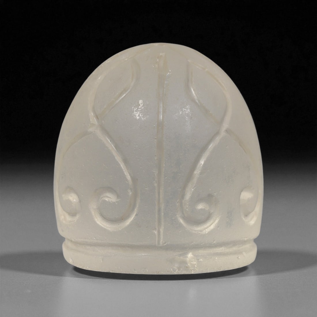 A Coptic Glass Carved Dome-Shaped Element, 4th-7th Century CE, 25LF: Formed from translucent glass with a pale, matte surface, the object is shaped as a dome with a flat base and a slightly rounded apex. Incised lines create a symmetrical arrangement of vertical and sc