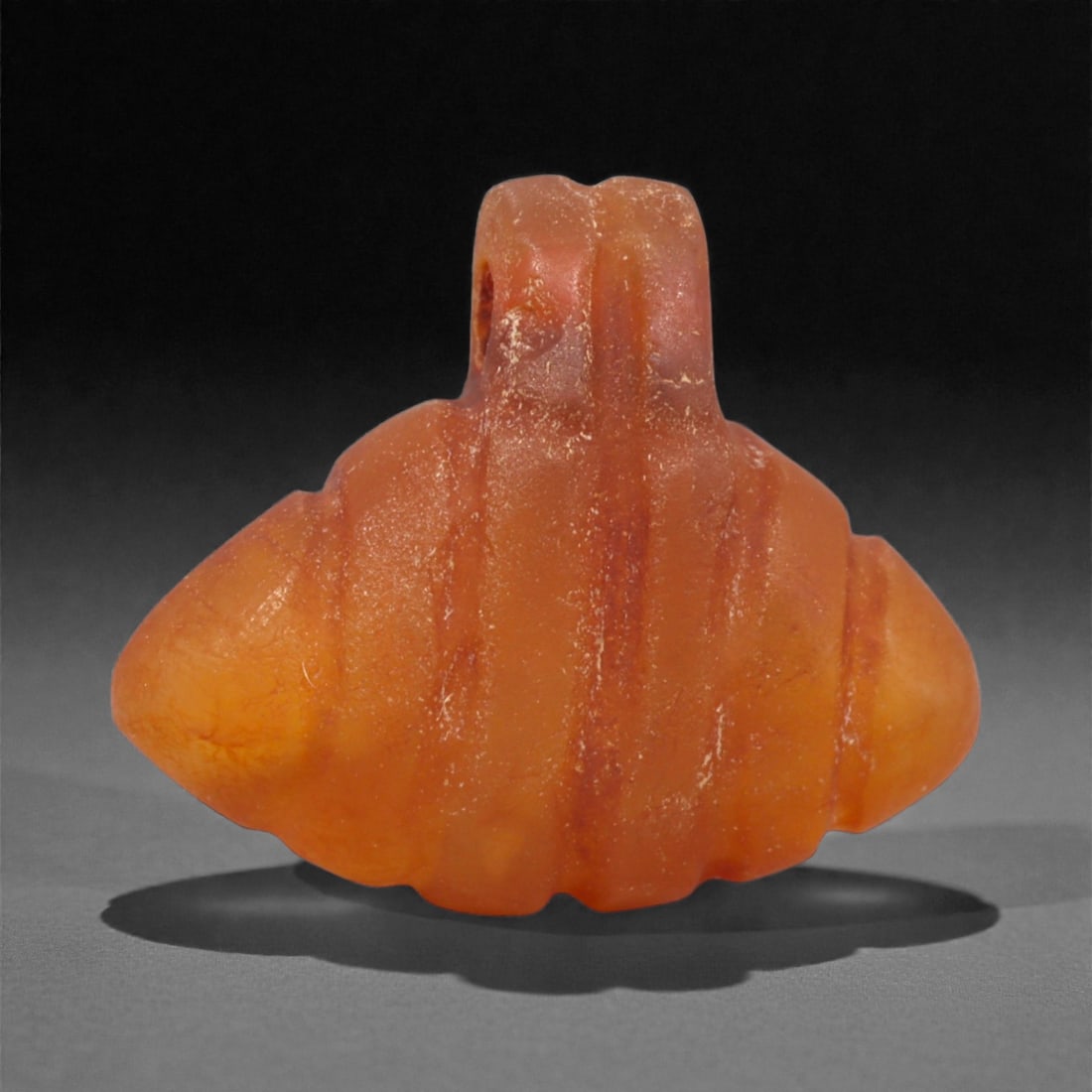 An Egyptian Carnelian Amulet, Coptic Period, 4th-7th Century CE, 1.8cm, 43LK: Worked from orange carnelian with natural internal variation, the amulet shows a compact form with smoothed contours and modest surface definition. Light wear is visible along the edges. Objects of th