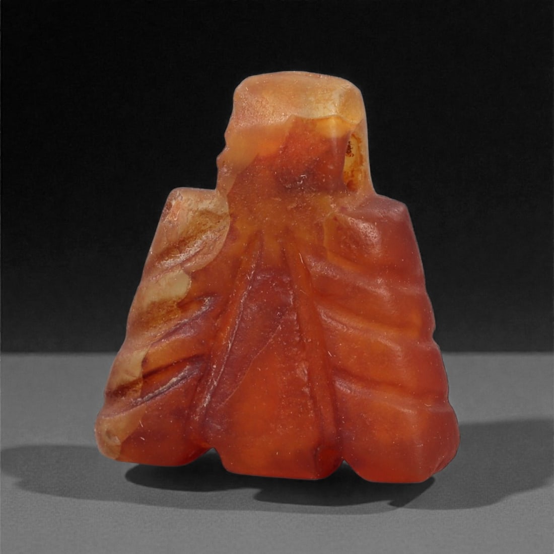 An Egyptian Carnelian Amulet, Coptic Period, 4th-7th Century CE, 1.5cm, 55LN: Worked from orange carnelian with natural internal variation, the amulet shows a compact form with smoothed contours and modest surface definition. Light wear is visible along the edges. Objects of th