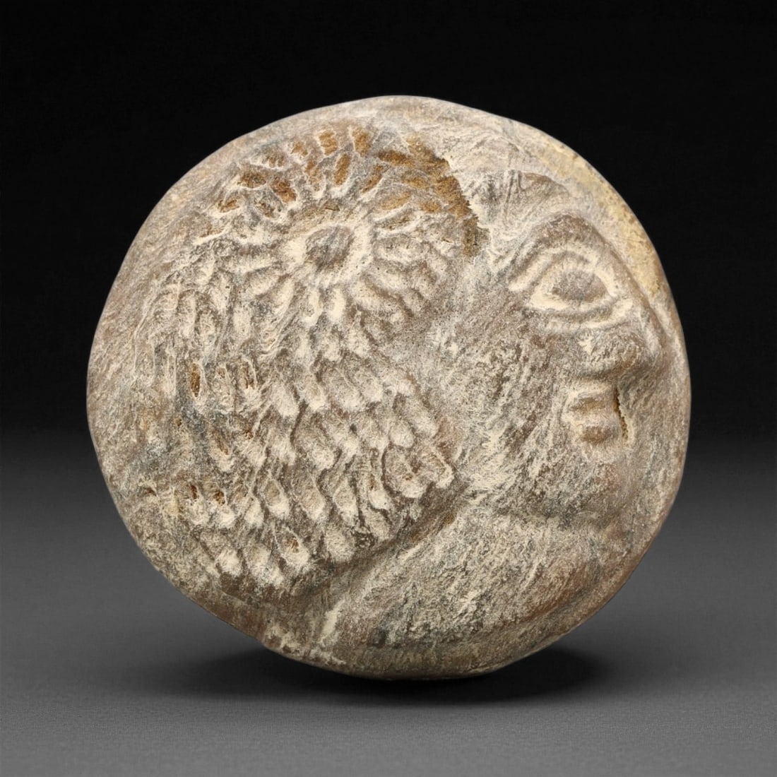 A Sasanian Stone Intaglio Plaque, 3rd-7th Century CE, 4.1cm, 49ET: The stone plaque is shaped with a convex surface bearing an incised profile head. The facial features are rendered with linear grooves defining the eye, brow, nose, and mouth, while additional incisio