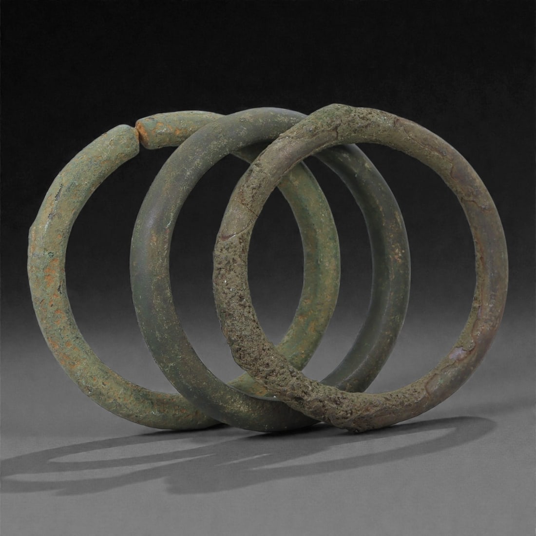Roman Bronze Bracelets, 1st-3rd Century CE, 23H: Cast in bronze with rounded circular profiles, the group comprises three open bracelets exhibiting green and brown patination with areas of surface accretion typical of burial conditions. Each bracele