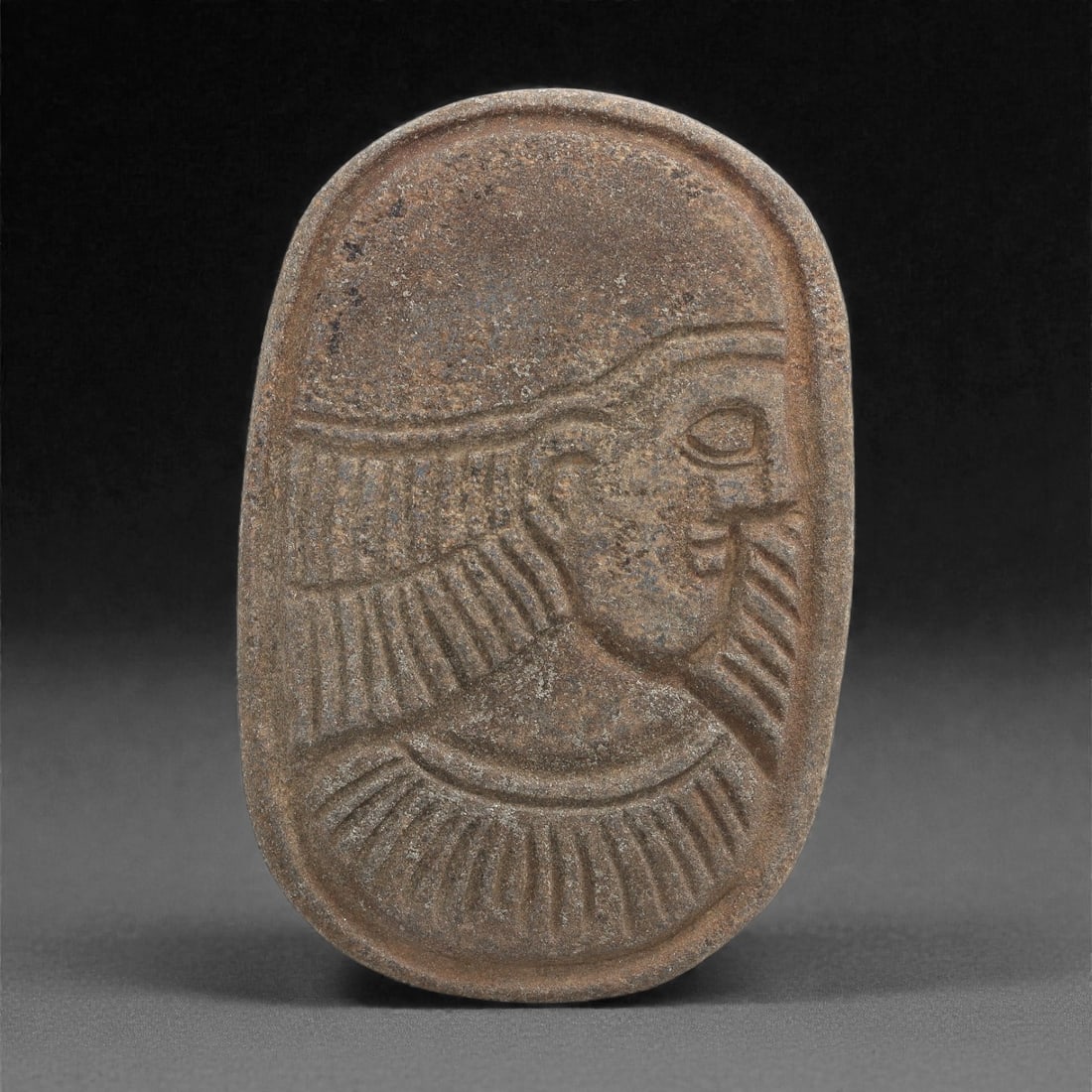 A Sasanian Lapis Lazuli Relief Plaque, 3rd-7th Century CE, 7.5cm, 75LQ: Carved from lapis lazuli with brown archaeological surface accretions, the plaque is worked in shallow relief exhibiting the characteristic linear incision and patterned surface treatment associated w