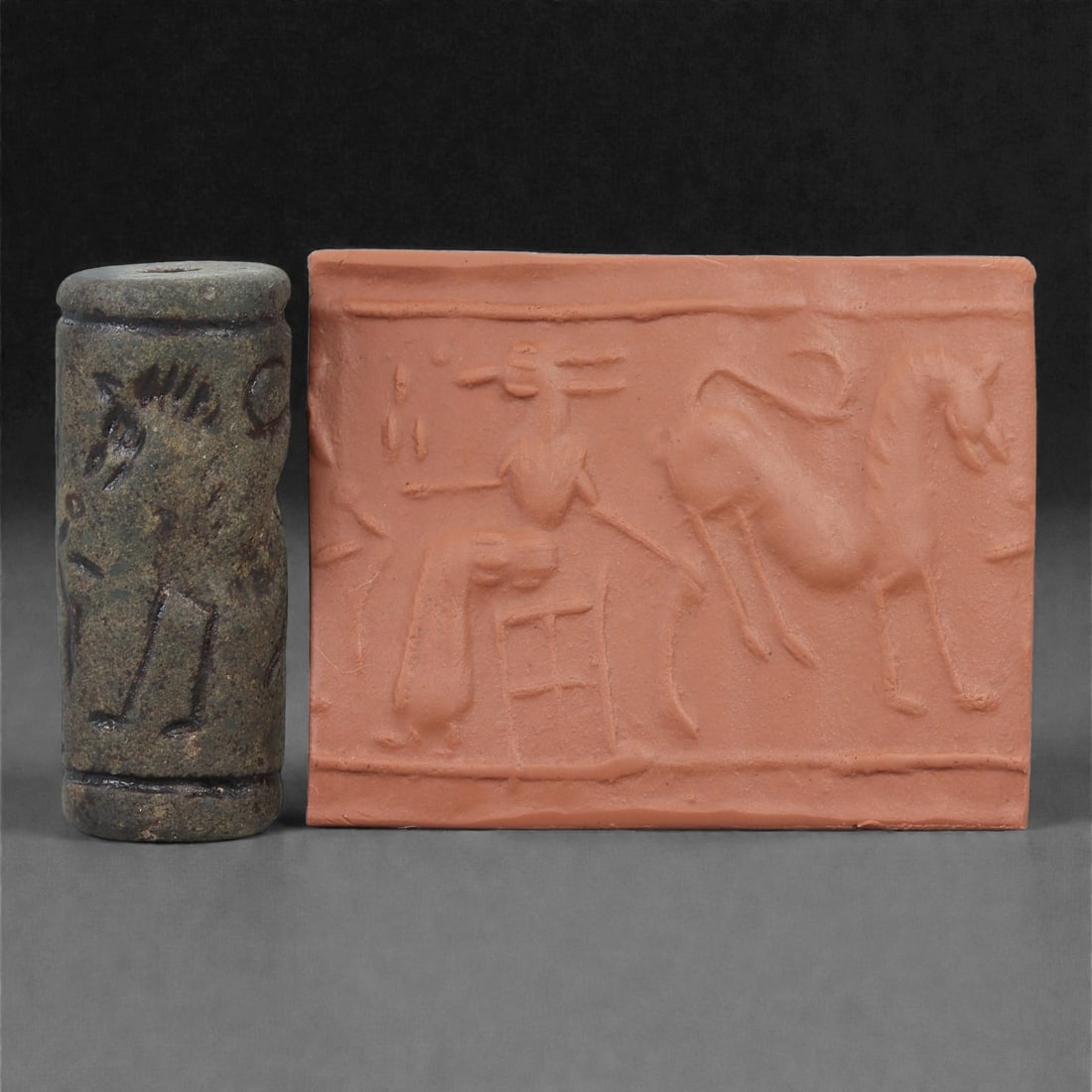 A Near Eastern Stone Cylinder Seal, 3rd Millennium BCE, 4.3cm, 29LH: Carved from stone with darker surface mottling, the cylindrical seal bears a continuous engraved scene. The carving is executed in shallow linear grooves typical of Early Bronze Age glyptic traditions