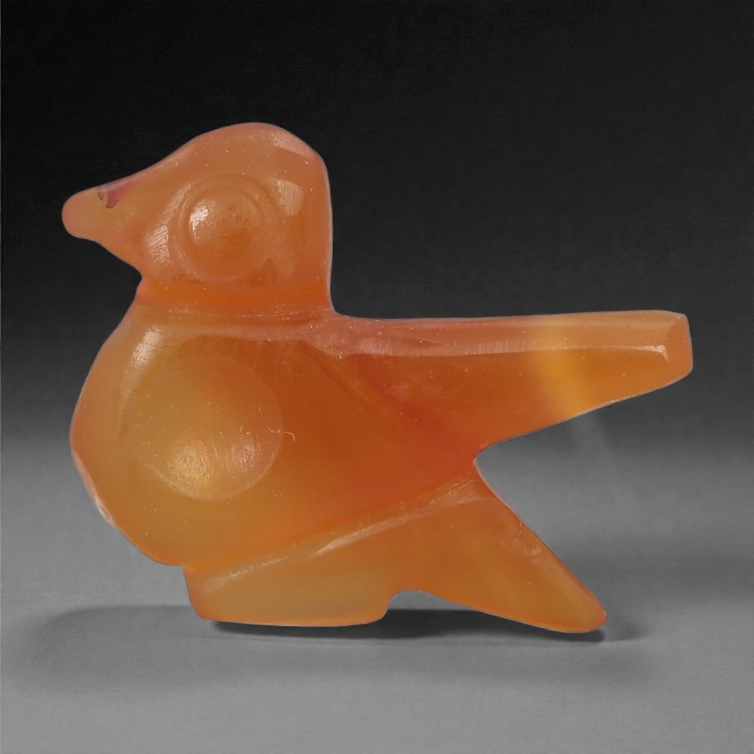 A Coptic Carnelian Bird Amulet, 4th-7th Century CE, 92LS: Carved from translucent orange carnelian with slight tonal variation, the amulet is formed as a stylized bird with a projecting beak, a circular recessed eye, and a long, tapering tail. The body is sm