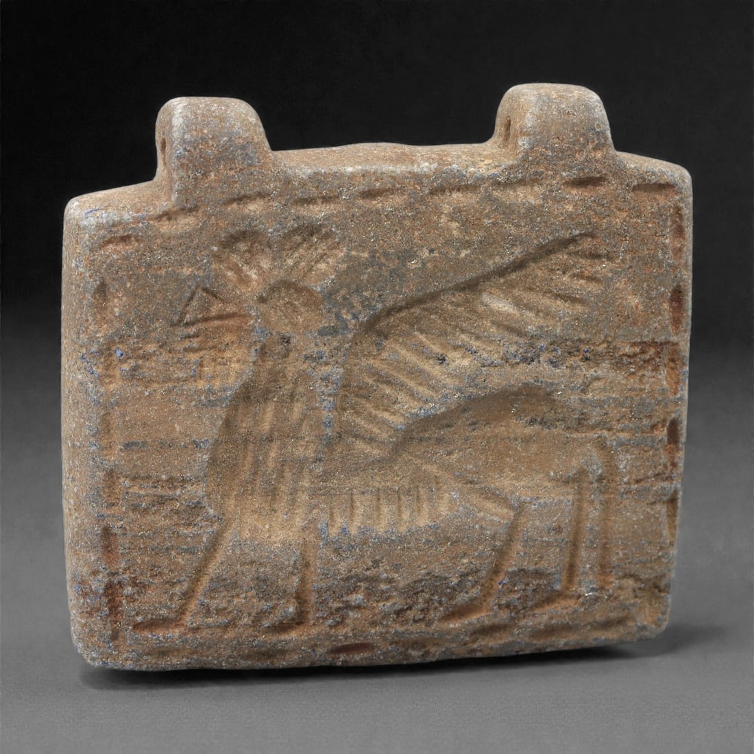 A Sasanian Lapis Lazuli Amulet, 3rd-7th Century CE, 4cm, 20LR: Carved from lapis lazuli with brown archaeological surface accretions, the amulet is worked in shallow relief employing the linear incision, patterned hatching, and schematic contouring characteristic