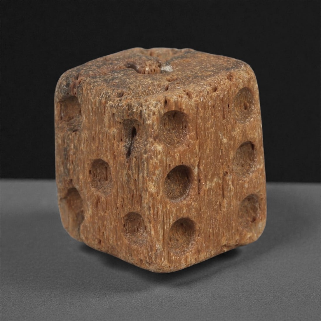 A Roman Bone Gaming Die, 1st-3rd Century CE, 1.4cm, 82AD: Carved from dense bone, the object is shaped as a small cube with slightly rounded edges. Each face bears a series of drilled circular pips arranged in standard numerical configurations. The surfaces 