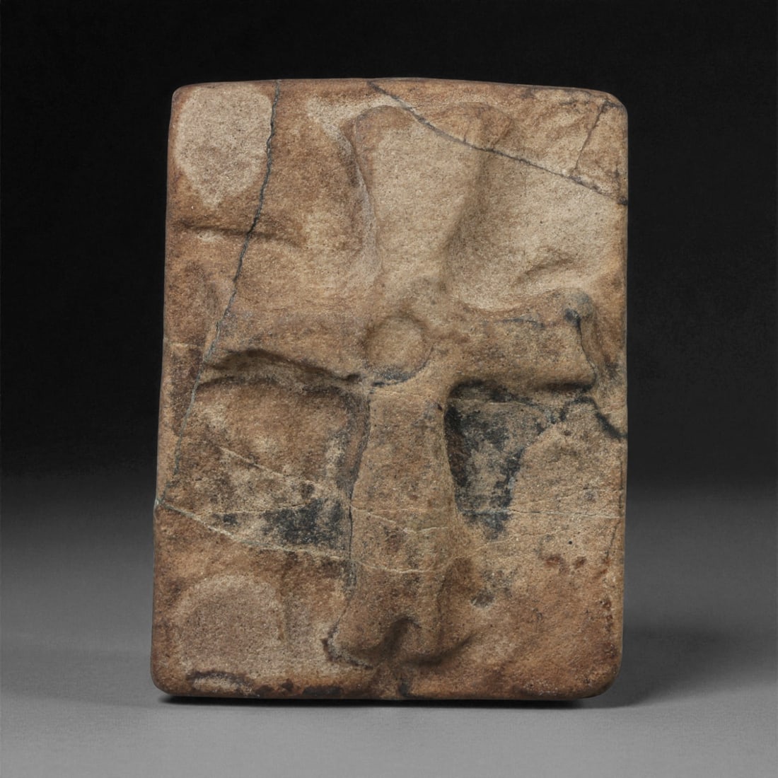 A Byzantine Stone Plaque with Incised Cross, 6th-8th Century CE, 51LA: Carved from light brown stone with darker surface inclusions, the plaque is rectangular with slightly rounded edges. The front bears a cross rendered in low relief, defined by broad recessed arms meet