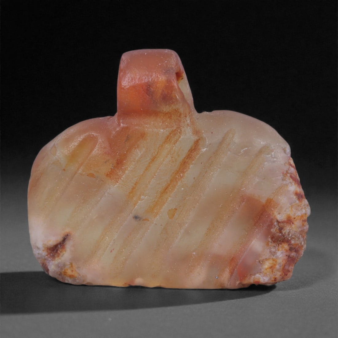 An Egyptian Carnelian Amulet, Coptic Period, 4th-7th Century CE, 1.9cm, 33Y: Worked from orange carnelian with natural internal variation, the amulet shows a compact form with smoothed contours and modest surface definition. Light wear is visible along the edges. Objects of th