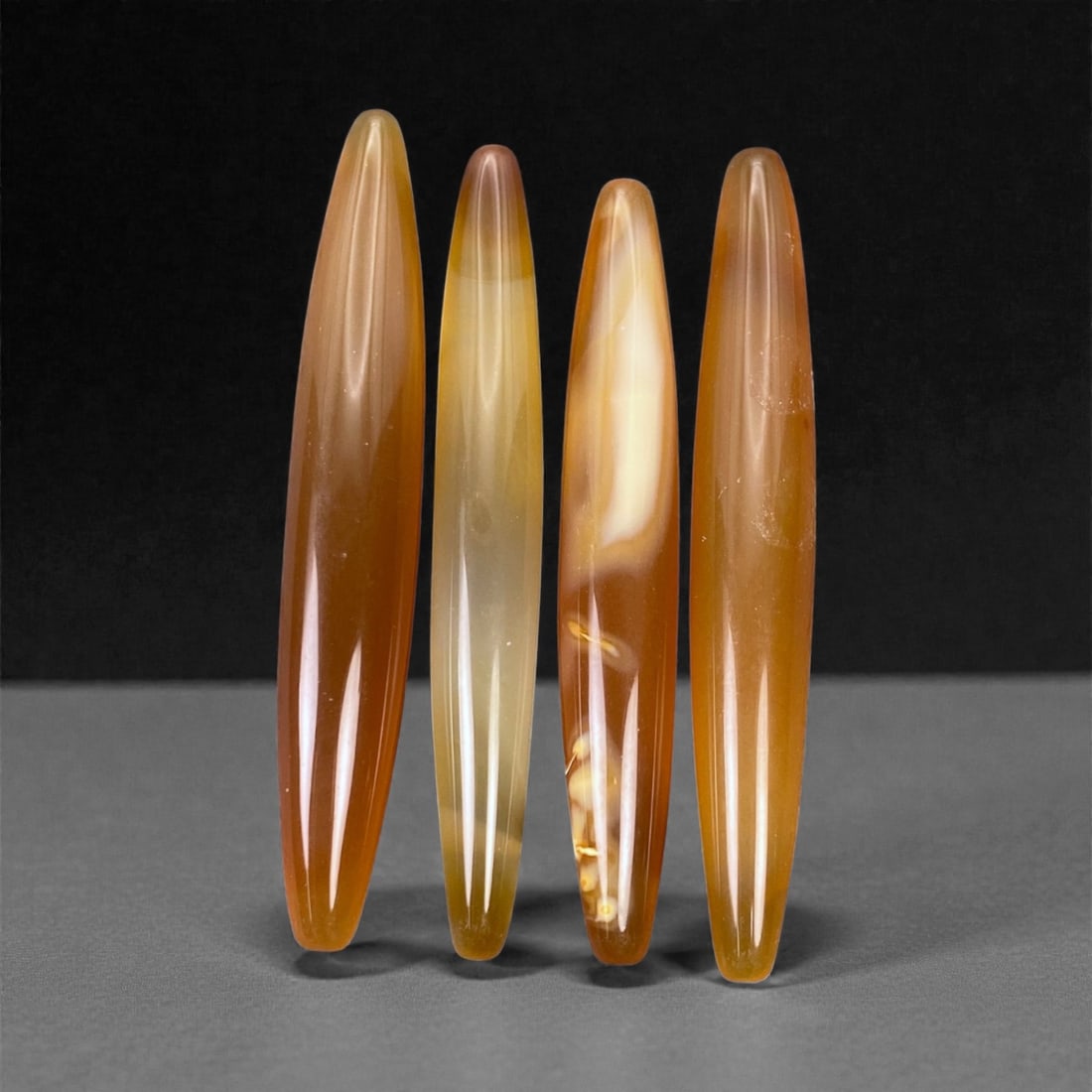Tibetan Carnelian Ritual Beads, 19th-20th Century CE, 5.6-6cm, 6L: Carved from translucent orange carnelian with natural internal banding, the group comprises elongated, double-conical elements with smoothly polished surfaces. Each bead is unperforated, indicating a 