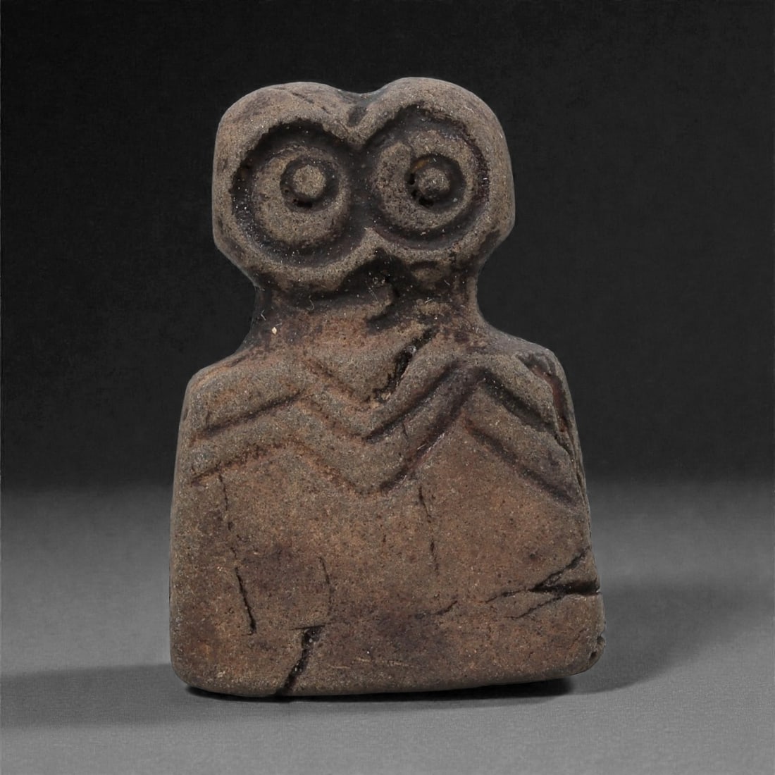 A Near Eastern Stone Eye Idol, 4th-3rd Millennium BCE, 50LH: Carved from a dark brown stone with scattered surface fissures, the figure is shaped with a squared lower body and a broad upper section bearing a pair of large circular eyes formed by recessed concen