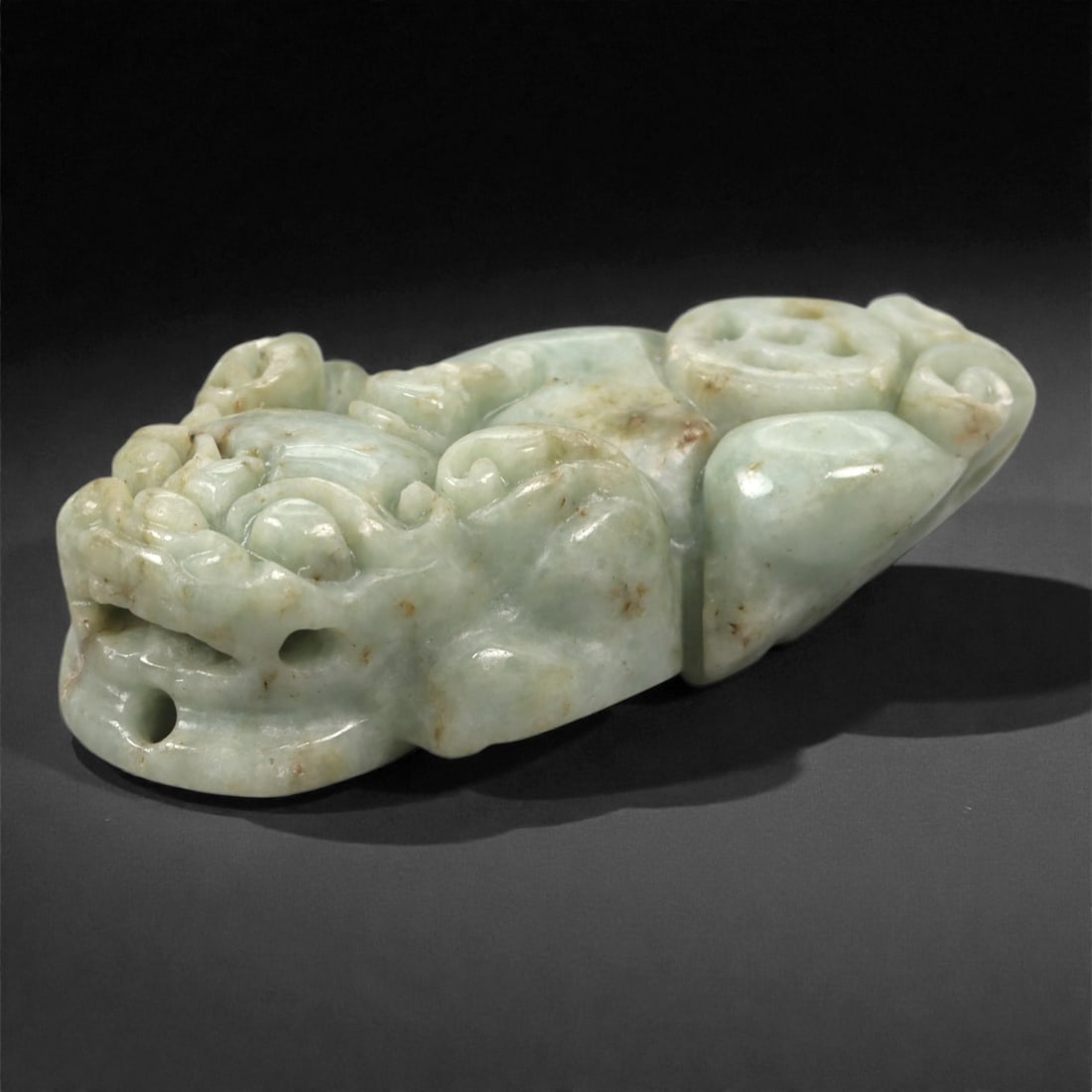 Chinese Jade Pixiu Amulet - Carved Stone Figure, 55P: Carved from pale green Chinese jade, this amulet depicts a stylized pixiu shown in a compact crouching posture, with rounded facial features, curled mane elements, and drilled perforations indicating