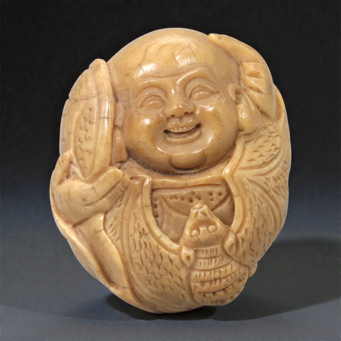 A Chinese Shell Carving of Budai, 20th Century, 21FC: Carved from pale-toned shell material, the object depicts Budai shown frontally with a rounded head, smiling expression, and exposed belly. The facial features are rendered in low relief, with arched 