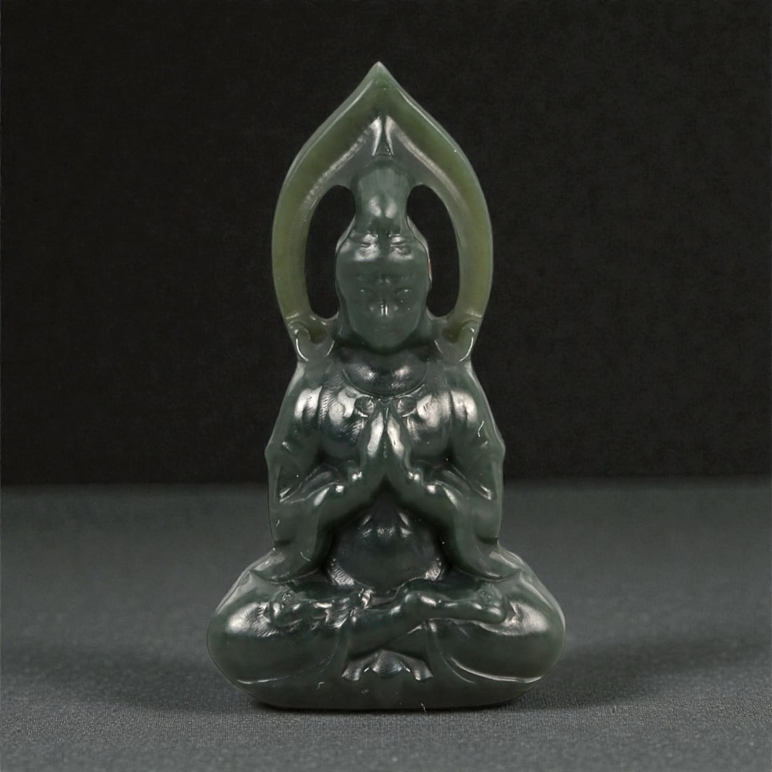 A Chinese Nephrite Jade Guanyin Figure, 20th Century, 48FA: Carved from dark green nephrite jade with areas of lighter translucency, the figure is modeled in the round as Guanyin seated in a meditative posture. The bodhisattva is shown cross-legged, with the h