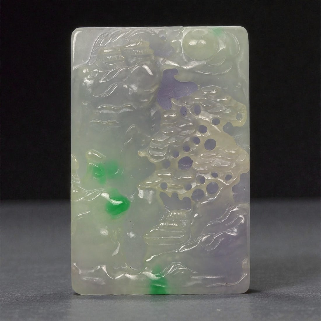 A Chinese Jadeite Jade Rectangular Plaque, 20th Century, 32FD: Carved from translucent pale jadeite with areas of lavender-grey and bright green inclusions, the object is worked as a rectangular plaque with a flat reverse and relief decoration on the front. The c