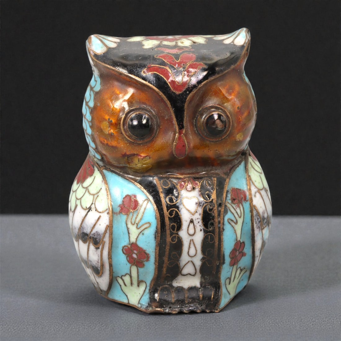 A Chinese Cloisonne Owl Effigy, 20th Century, 61FC: Constructed from a copper alloy body and decorated in cloisonne enamel, the object is formed as a standing owl rendered in a compact, frontal pose. The head is broad with pronounced circular eyes mode