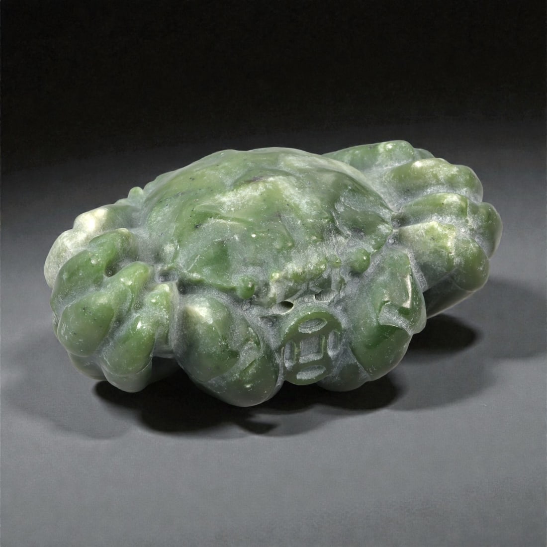 A Chinese Jade Toad Sculpture, 20th Century, 82YA: Carved from green jade with areas of lighter mottling and natural translucency, the sculpture represents a crouching toad modeled fully in the round. The creature is shown with a compact, rounded body