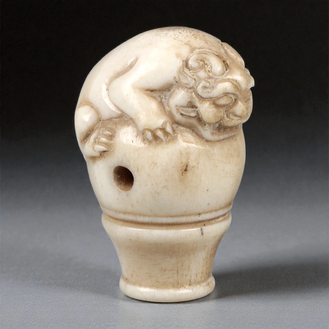 An East Asian Bone Bead with Zoomorphic Finial, 19th-20th Century, 97FC: Carved from bone of pale cream tone with areas of darker patination, the bead is formed with a baluster-shaped lower section surmounted by a sculpted zoomorphic figure. The animal, rendered in compact