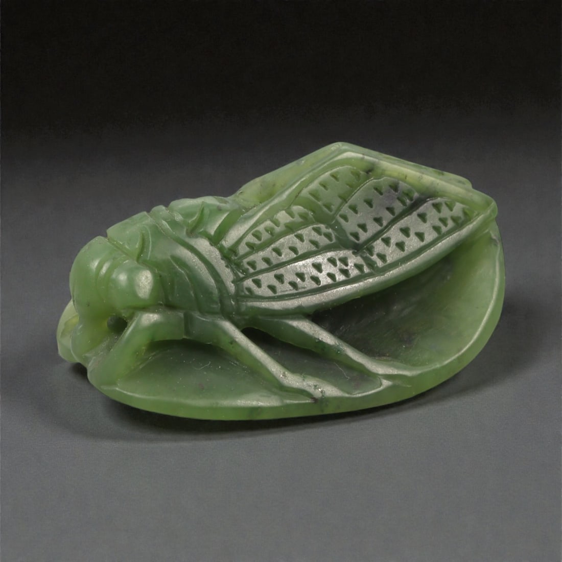 A Chinese Jade Cicada Carving, 20th Century, 8FB: Carved from dark green jade with lighter mottling and areas of mild translucency, the object represents a cicada shown in repose. The insect is rendered in low relief, with the body aligned along the