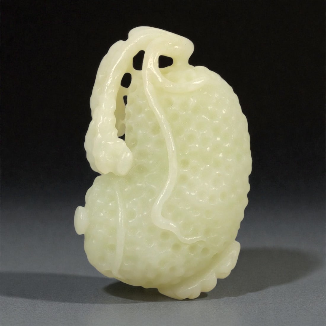 A Chinese Nephrite Jade Fruit Pendant, 20th Century, 75FA: Carved from pale celadon nephrite jade with a high degree of translucency and fine natural clouding, the pendant is worked in relief to depict a fruiting vine, likely gourds or melons, arranged in a c