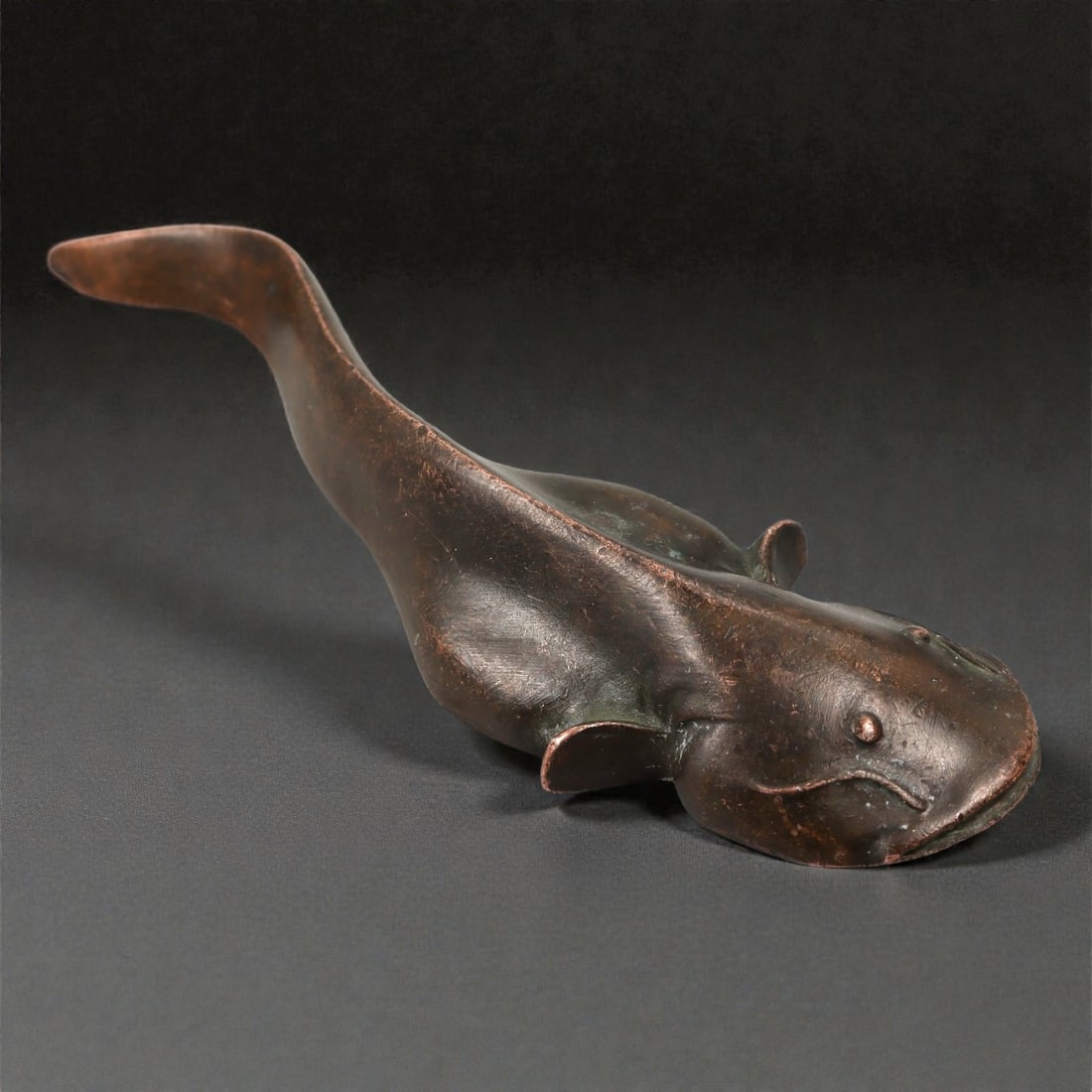 A Chinese Bronze Catfish Figure, Qing Dynasty, 18th-19th Century, 16YB: Cast in bronze, the figure represents a catfish shown resting on its belly with the elongated body curving gently toward an upturned tail. The head is flattened and broad, with rounded eyes set high o