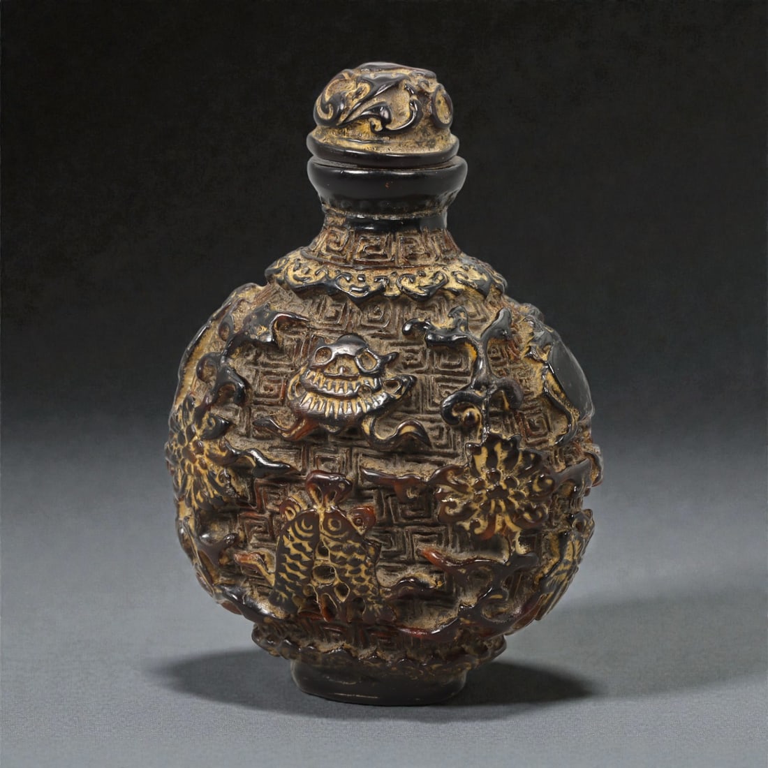 A Chinese Amber Snuff Bottle, 20th Century, 58FC: Carved from translucent amber of dark honey-brown tone with areas of lighter inclusions, the snuff bottle is of compressed ovoid form rising from a short, circular foot to a narrow neck with a fitted