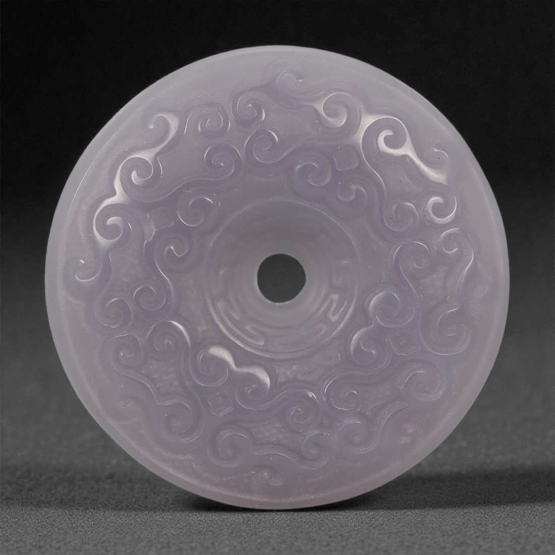 A Chinese Hetian Jade Bi Disc, 20th Century, 68FD: Carved from pale lavender-toned Hetian jade with soft translucency, the disc is worked as a circular bi form with a central perforation. Both faces are decorated in shallow relief with continuous scro
