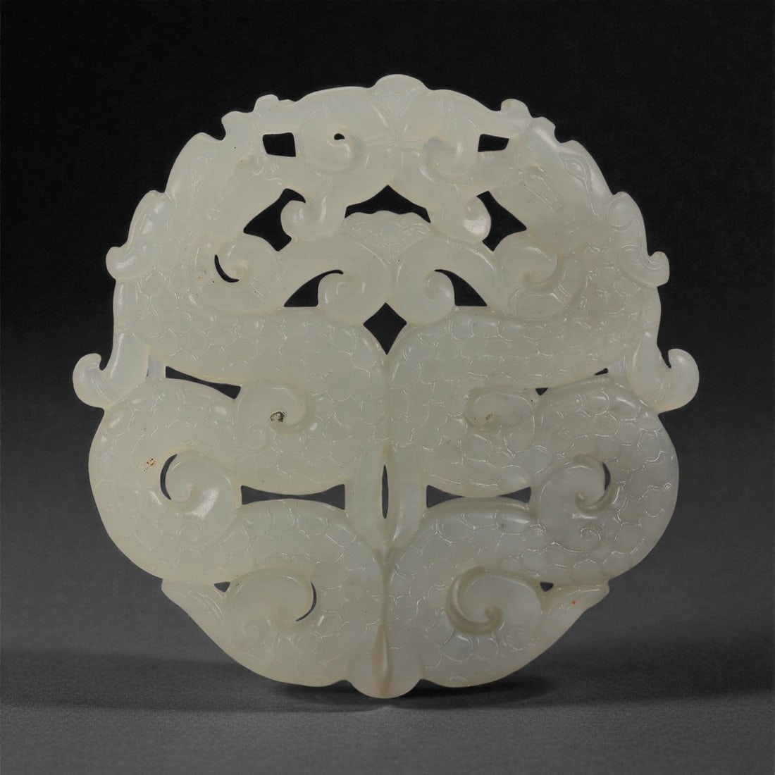 A Chinese White Nephrite Jade Openwork Plaque, 20th Century, 63FD: Carved from pale white nephrite jade of even tone with a soft, lustrous polish. The plaque is formed as a flattened oval with symmetrical openwork decoration on both faces. The design comprises confro